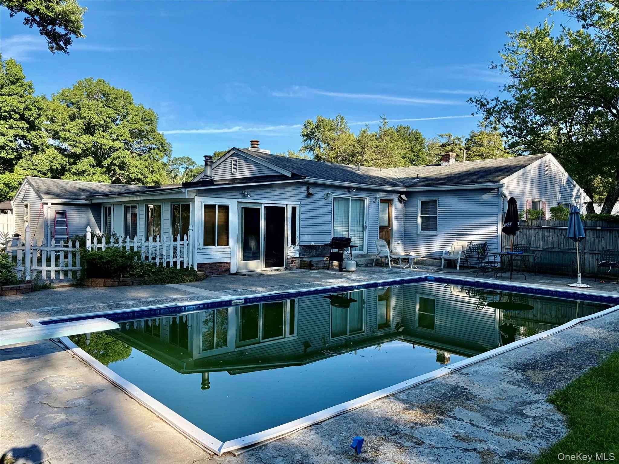 In-ground swimming pool with diving board, sunroom with sliding glass doors, and a white picket fence In-ground swimming pool with diving board, sunroom with sliding glass doors, and a white picket fence