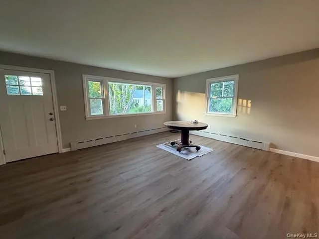 Unfurnished living room featuring baseboard heating, healthy amount of natural light, and wood finished floors. Unfurnished living room featuring baseboard heating, healthy amount of natural light, and wood finished floors.