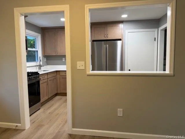 Kitchen with freestanding refrigerator, gas stove, light wood-type flooring, light countertops, and recessed lighting. Kitchen with freestanding refrigerator, gas stove, light wood-type flooring, light countertops, and recessed lighting.