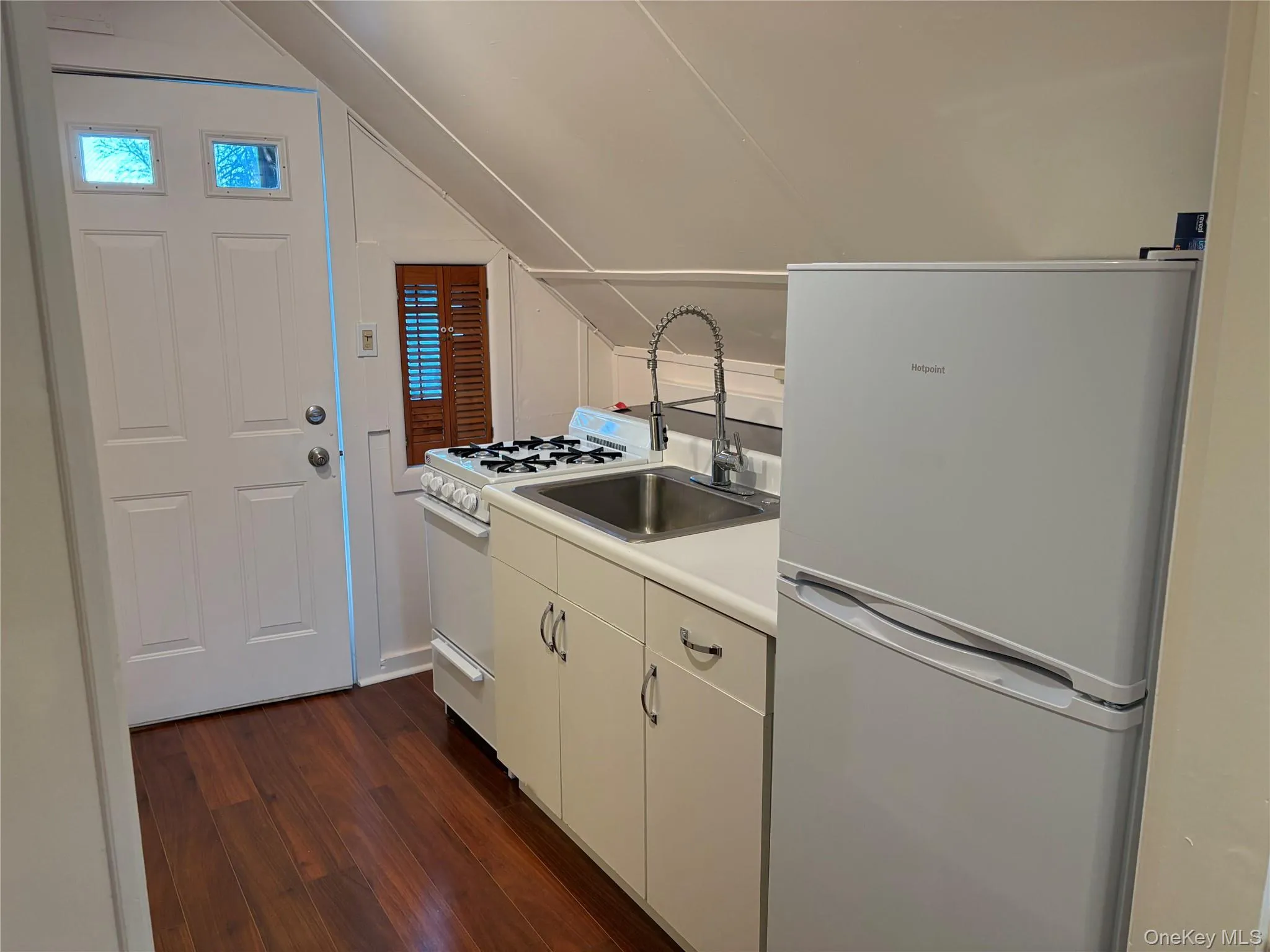 Kitchen with lofted ceiling, sink, white cabinetry, dark hardwood / wood-style floors, and white appliances Kitchen with lofted ceiling, sink, white cabinetry, dark hardwood / wood-style floors, and white appliances