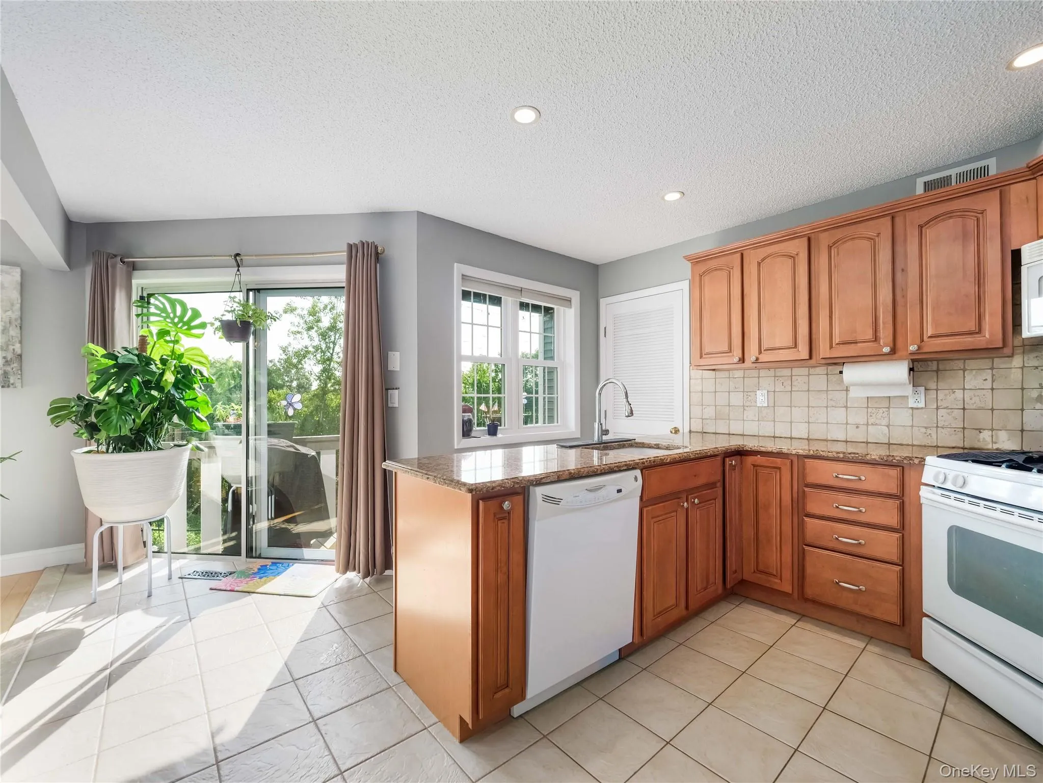 Kitchen featuring wood cabinetry, stone-finish countertops, tiled backsplash, recessed ceiling lighting, and sliding glass doors Kitchen featuring wood cabinetry, stone-finish countertops, tiled backsplash, recessed ceiling lighting, and sliding glass doors