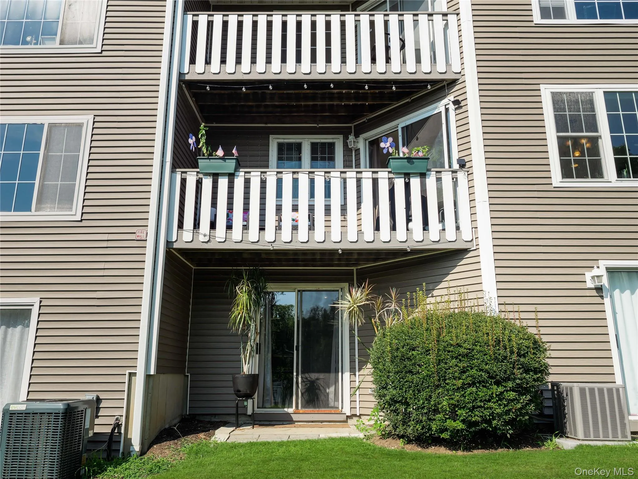 Exterior vinyl siding featuring a private balcony with white railings, sliding glass doors, and a ground-level concrete patio Exterior vinyl siding featuring a private balcony with white railings, sliding glass doors, and a ground-level concrete patio