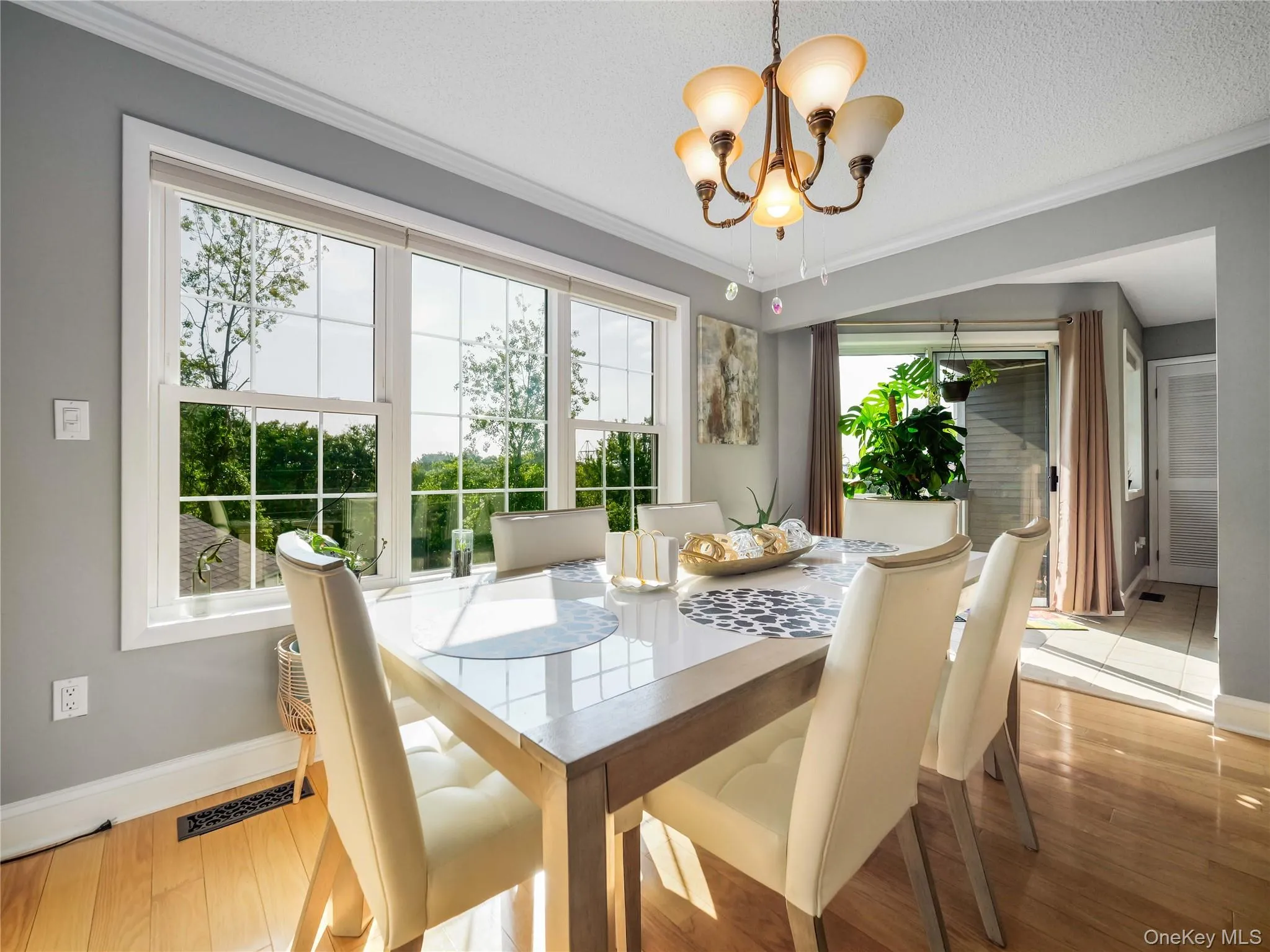 Dining area featuring light-toned wood-finish flooring, crown molding, multi-pane windows, and a multi-arm chandelier Dining area featuring light-toned wood-finish flooring, crown molding, multi-pane windows, and a multi-arm chandelier