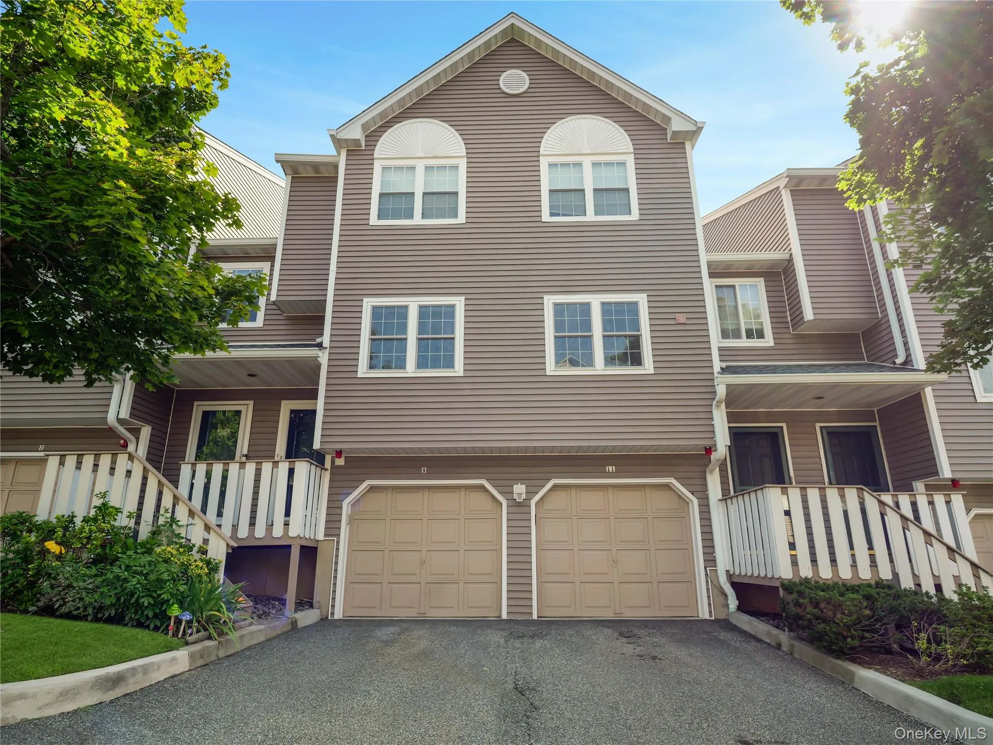 Multi-level exterior featuring light-gray horizontal siding, arched upper-story windows, double attached garage, and raised wooden railings Multi-level exterior featuring light-gray horizontal siding, arched upper-story windows, double attached garage, and raised wooden railings