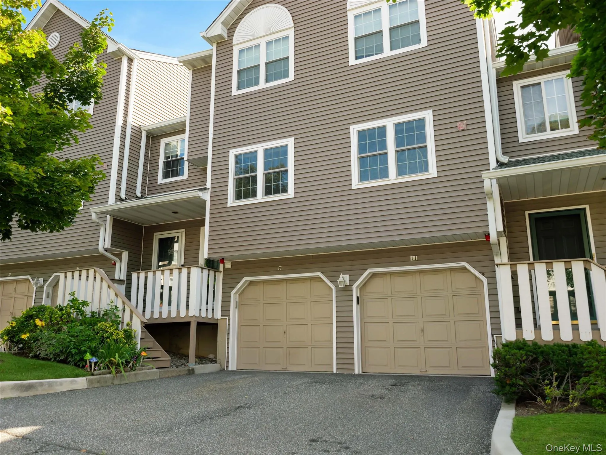 Multi-story townhouse exterior featuring horizontal siding, double-garage configuration with paneled doors, and elevated entryways with wood-composite railings Multi-story townhouse exterior featuring horizontal siding, double-garage configuration with paneled doors, and elevated entryways with wood-composite railings