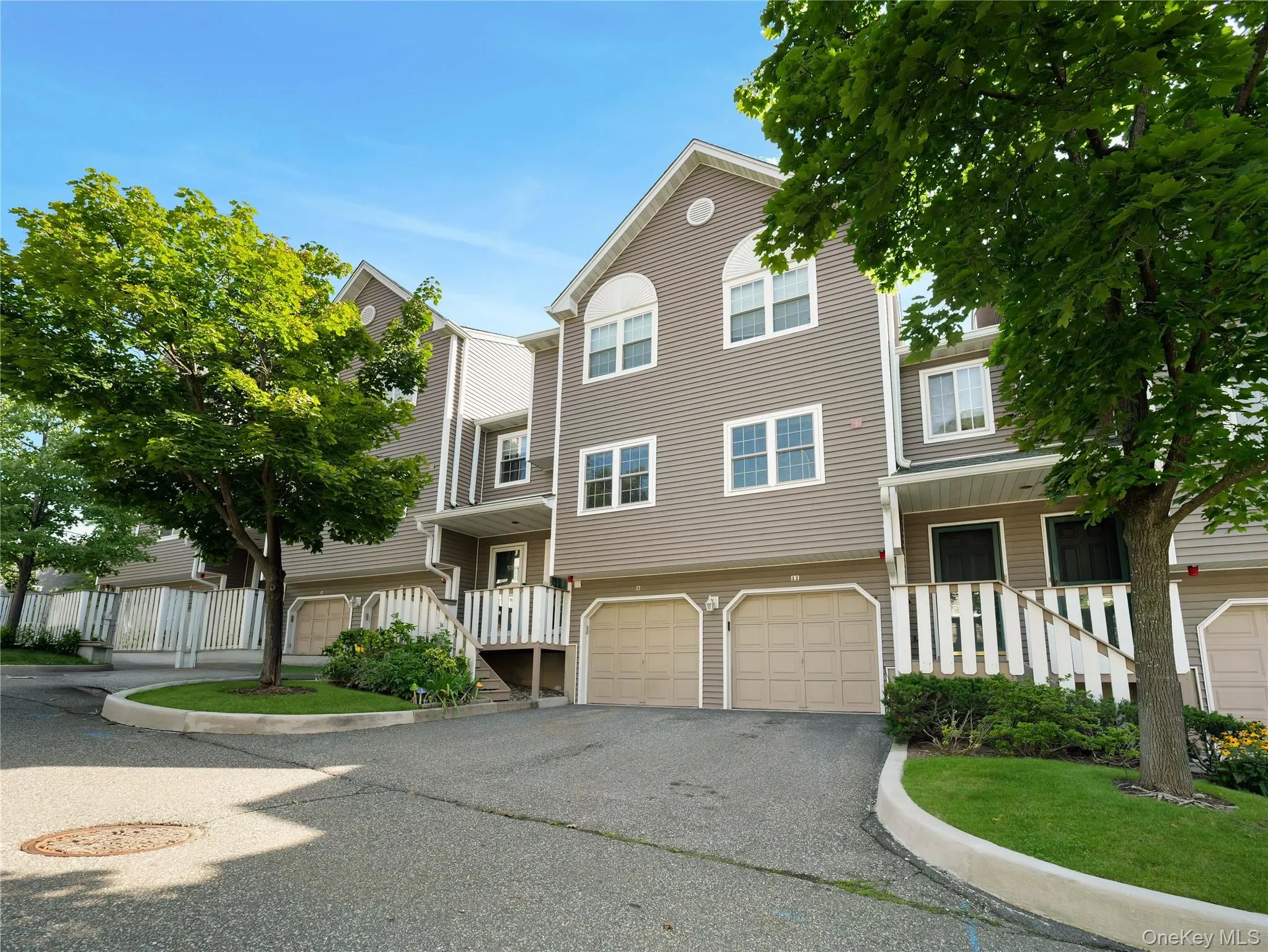 Multi-level townhouse exterior featuring vinyl siding, gable rooflines, arched window accents, attached two-car garages, and white rail-style stair railings Multi-level townhouse exterior featuring vinyl siding, gable rooflines, arched window accents, attached two-car garages, and white rail-style stair railings