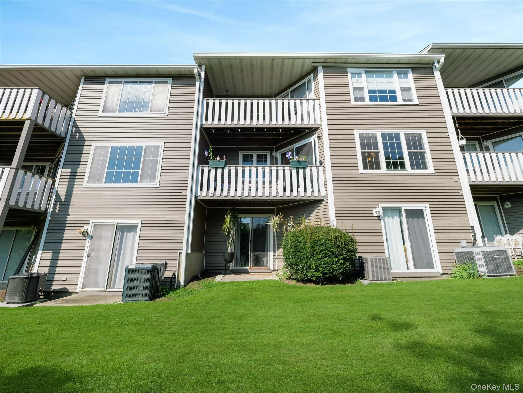 Multi-story residential exterior featuring horizontal vinyl siding, elevated private balconies with vertical railings, sliding glass doors, and manicured lawn space Multi-story residential exterior featuring horizontal vinyl siding, elevated private balconies with vertical railings, sliding glass doors, and manicured lawn space