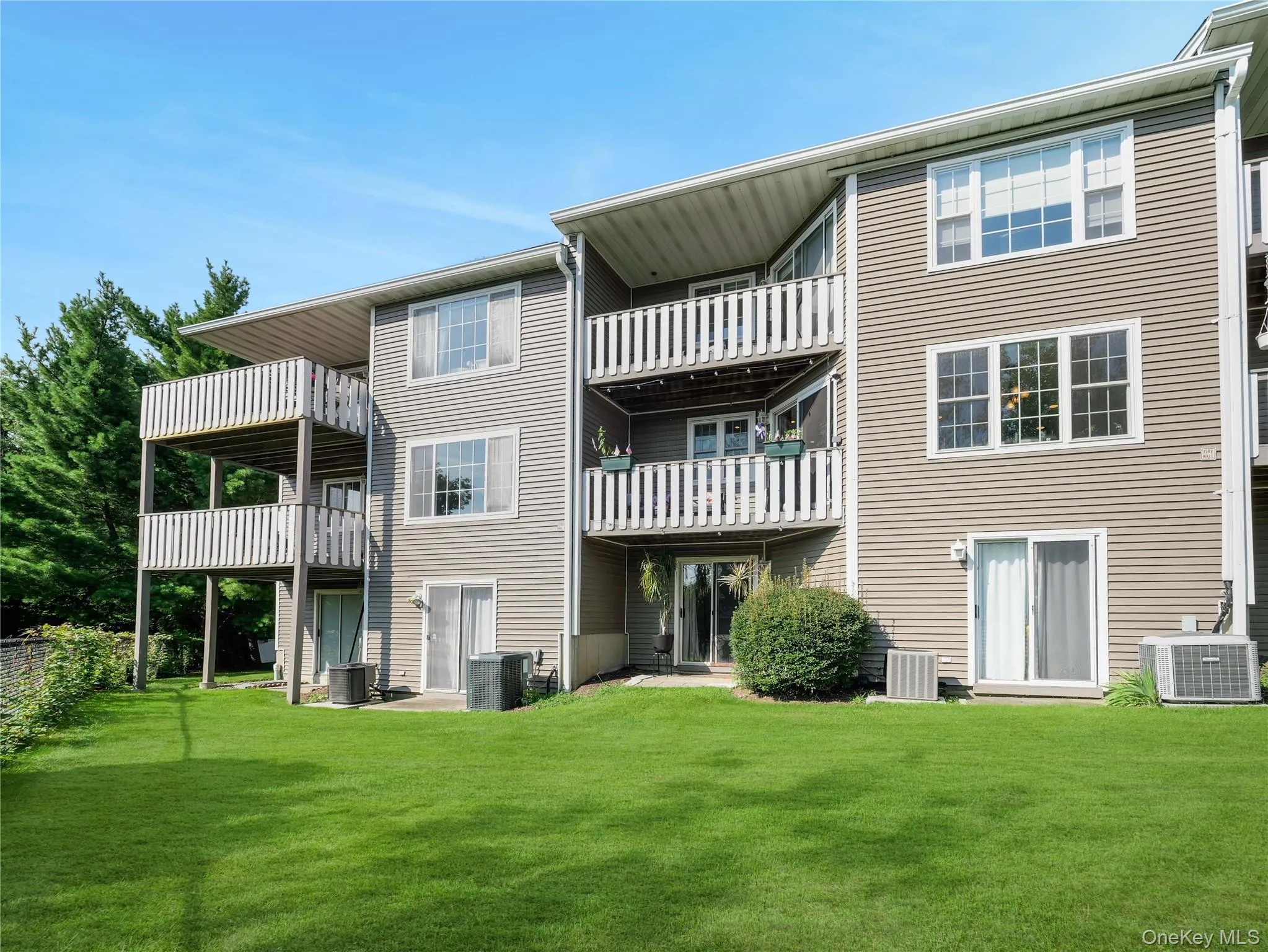 Multi-level exterior featuring horizontal siding, multiple stacked balconies with white railings, sliding glass doors, and an expansive lawn Multi-level exterior featuring horizontal siding, multiple stacked balconies with white railings, sliding glass doors, and an expansive lawn