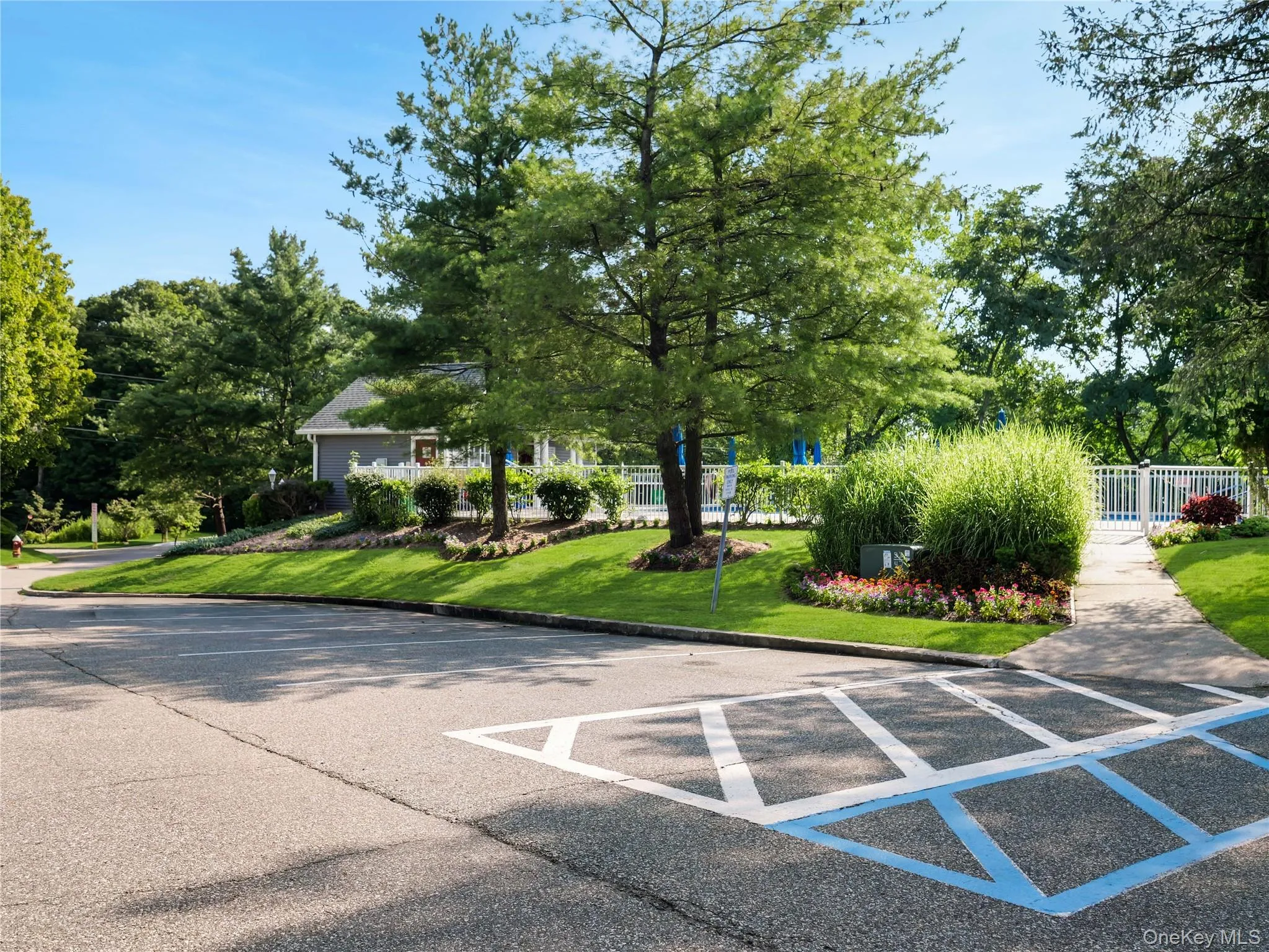 Asphalt parking area with designated markings, manicured lawn, established shade trees, perimeter fencing, and concrete walkway Asphalt parking area with designated markings, manicured lawn, established shade trees, perimeter fencing, and concrete walkway