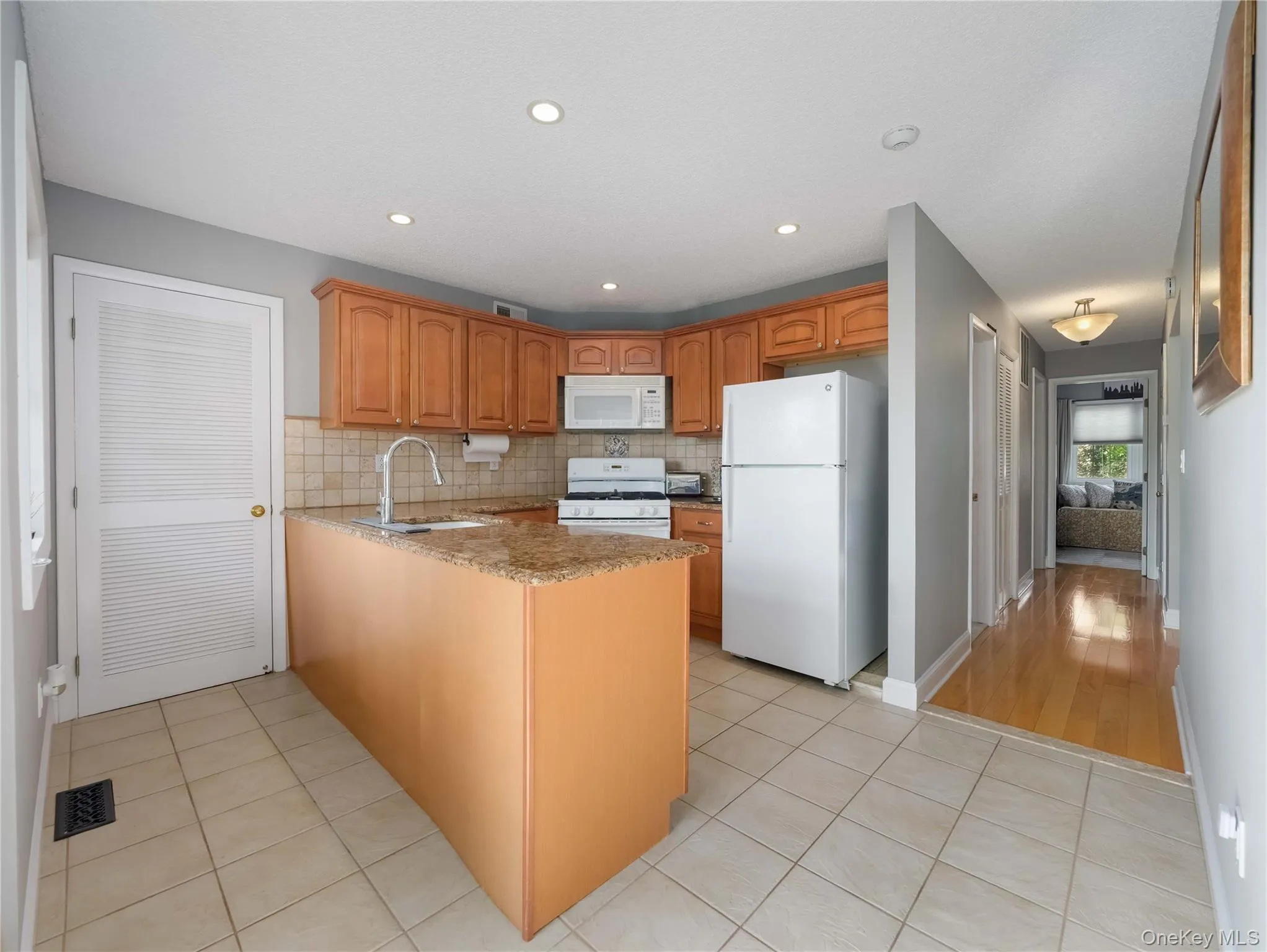 Kitchen featuring a peninsula with stone-finish countertops, wood cabinetry, tile flooring, and recessed lighting Kitchen featuring a peninsula with stone-finish countertops, wood cabinetry, tile flooring, and recessed lighting