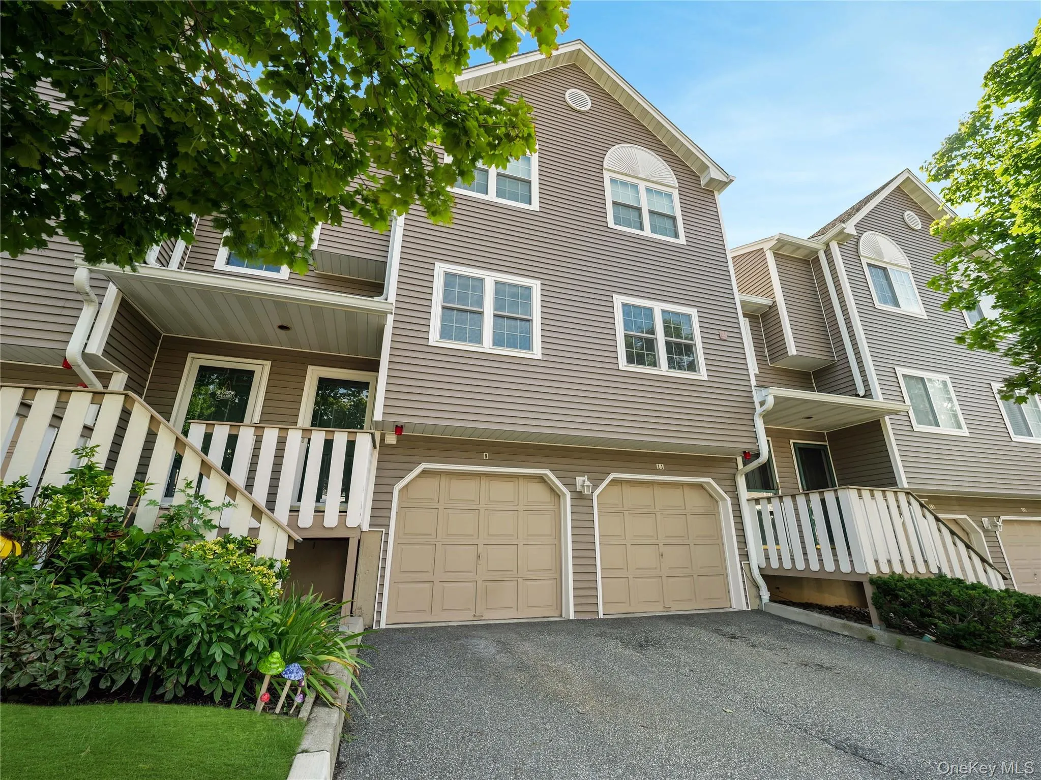 Multi-level exterior featuring horizontal vinyl siding, dual attached garage bays, raised entry porches with white railings, and arched window detailing Multi-level exterior featuring horizontal vinyl siding, dual attached garage bays, raised entry porches with white railings, and arched window detailing