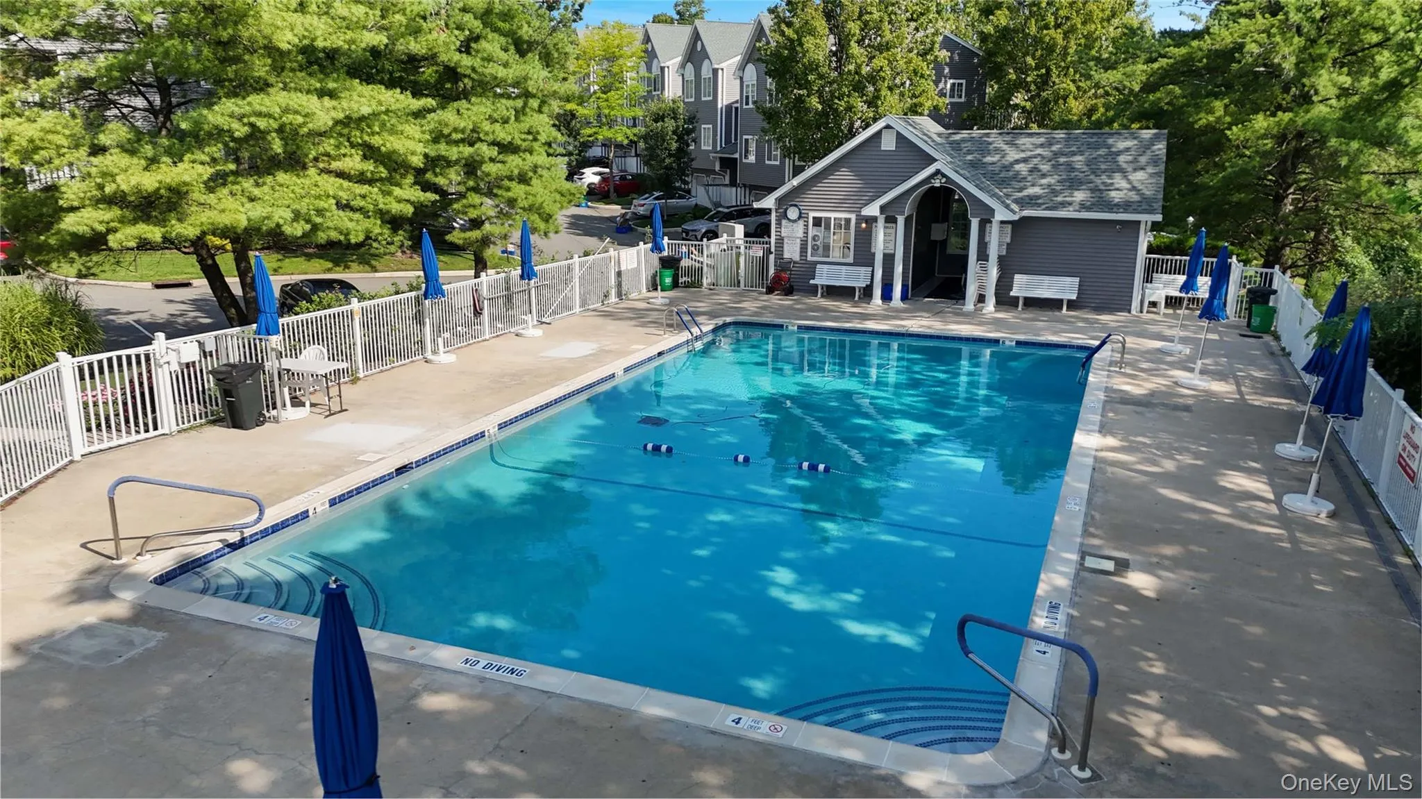In-ground swimming pool featuring a concrete deck, built-in steps, and a perimeter safety fence In-ground swimming pool featuring a concrete deck, built-in steps, and a perimeter safety fence