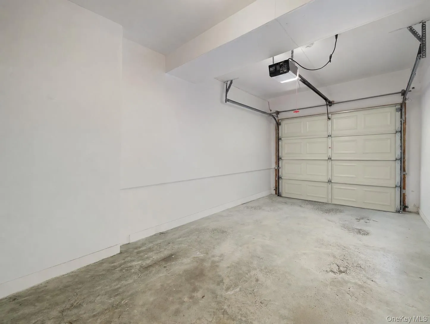 Enclosed garage space featuring high-finish white walls, concrete flooring, and an automated overhead door system Enclosed garage space featuring high-finish white walls, concrete flooring, and an automated overhead door system