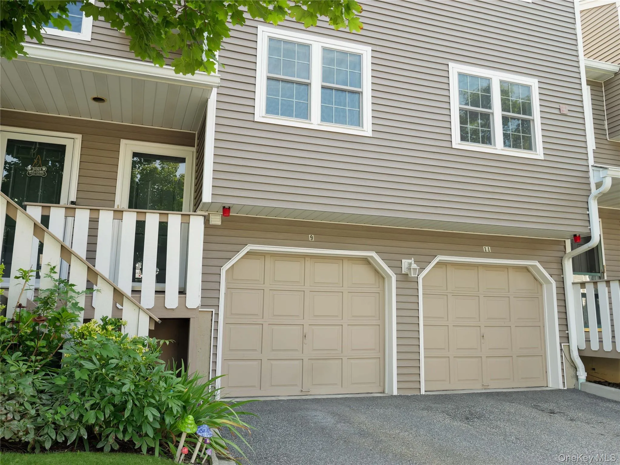 Multi-level exterior featuring light-toned horizontal siding, a dual-bay garage with raised-panel doors, and an elevated entry staircase with vertical balusters Multi-level exterior featuring light-toned horizontal siding, a dual-bay garage with raised-panel doors, and an elevated entry staircase with vertical balusters