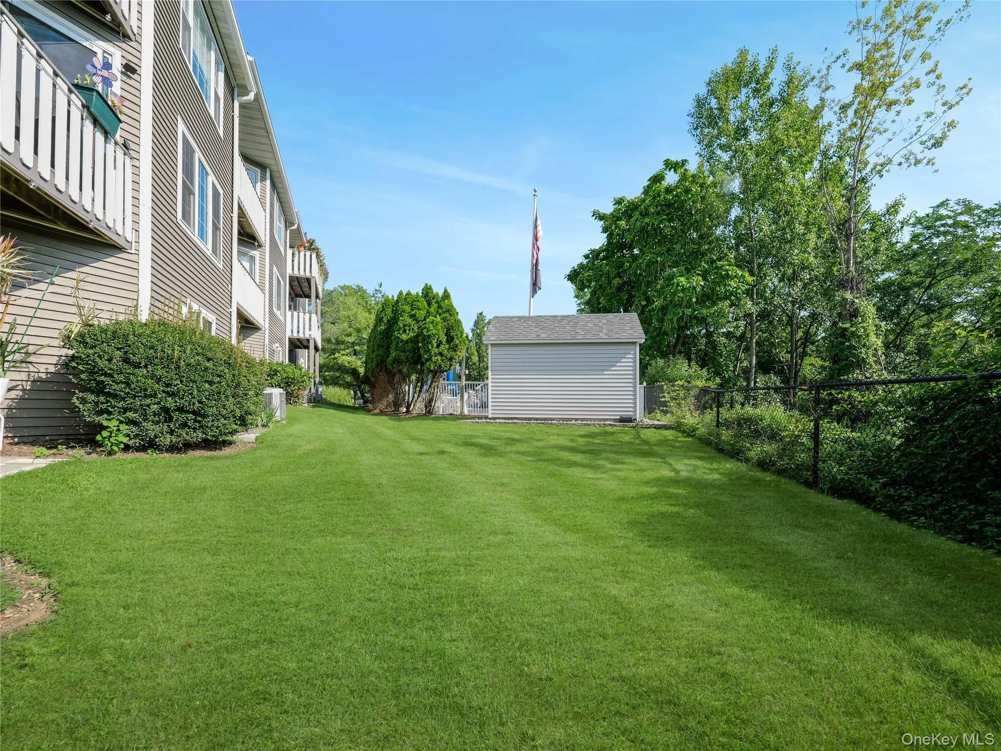 Expansive lawn featuring a detached storage shed, mature perimeter landscaping, and chain-link fencing Expansive lawn featuring a detached storage shed, mature perimeter landscaping, and chain-link fencing