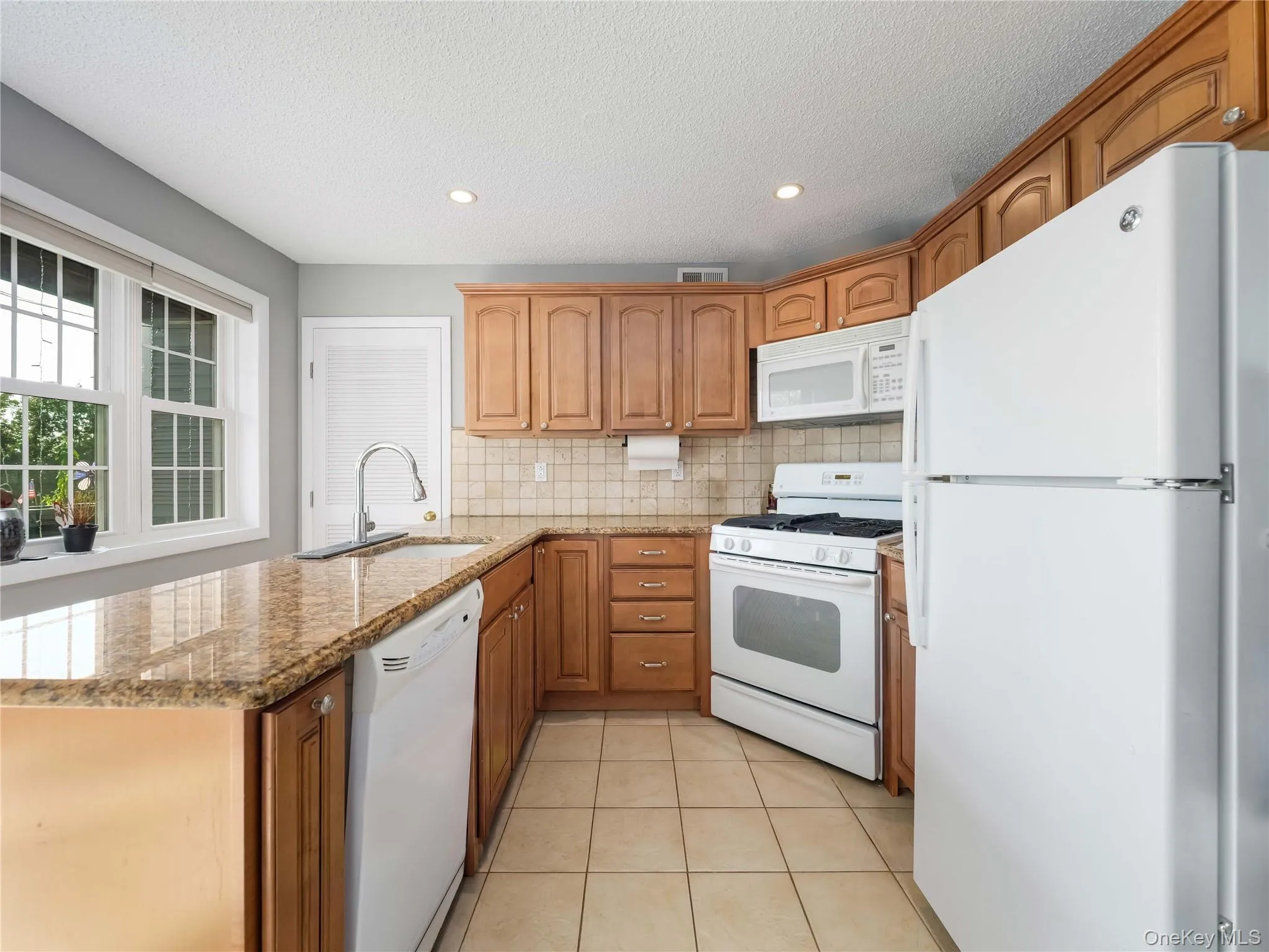 Kitchen featuring raised-panel wood cabinetry, stone countertops, tile backsplash, tile flooring, and white appliances Kitchen featuring raised-panel wood cabinetry, stone countertops, tile backsplash, tile flooring, and white appliances