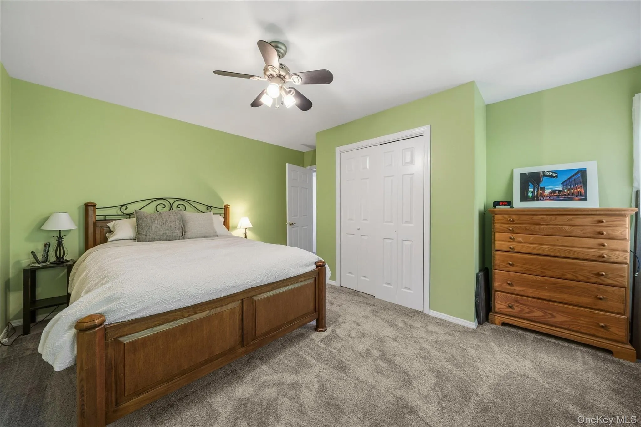 Plush gray carpet, wood-finish bed frame, and a ceiling fan with integrated lighting Plush gray carpet, wood-finish bed frame, and a ceiling fan with integrated lighting