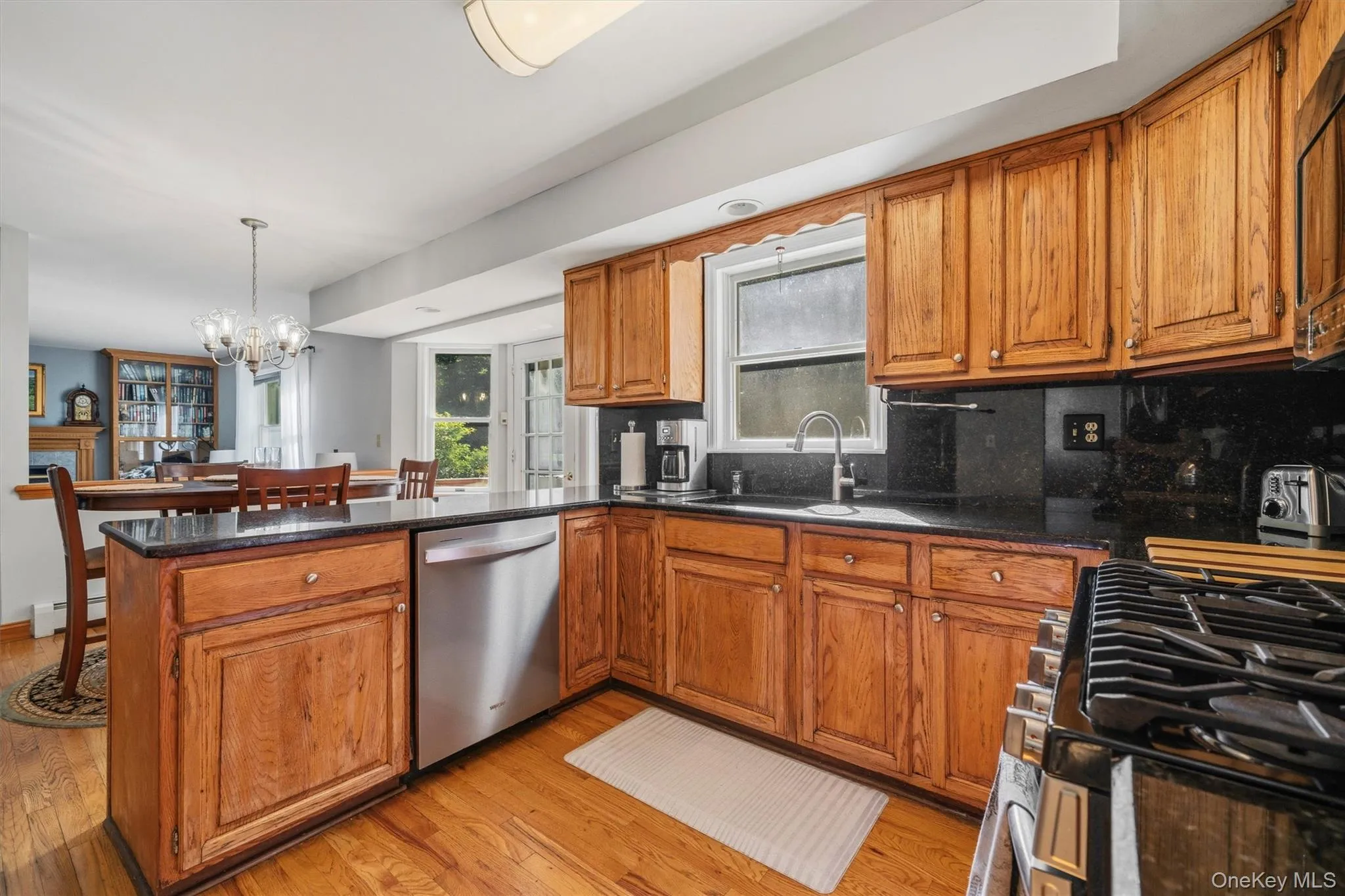 Kitchen featuring wood-finish cabinetry, black countertops, stainless steel dishwasher, and a gas range Kitchen featuring wood-finish cabinetry, black countertops, stainless steel dishwasher, and a gas range
