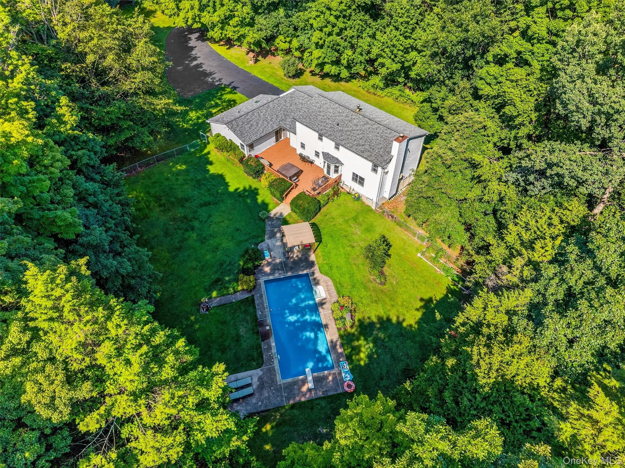 Expansive property featuring a paved driveway, mature trees, a swimming pool with a concrete surround, and a multi-level wood-finish deck Expansive property featuring a paved driveway, mature trees, a swimming pool with a concrete surround, and a multi-level wood-finish deck