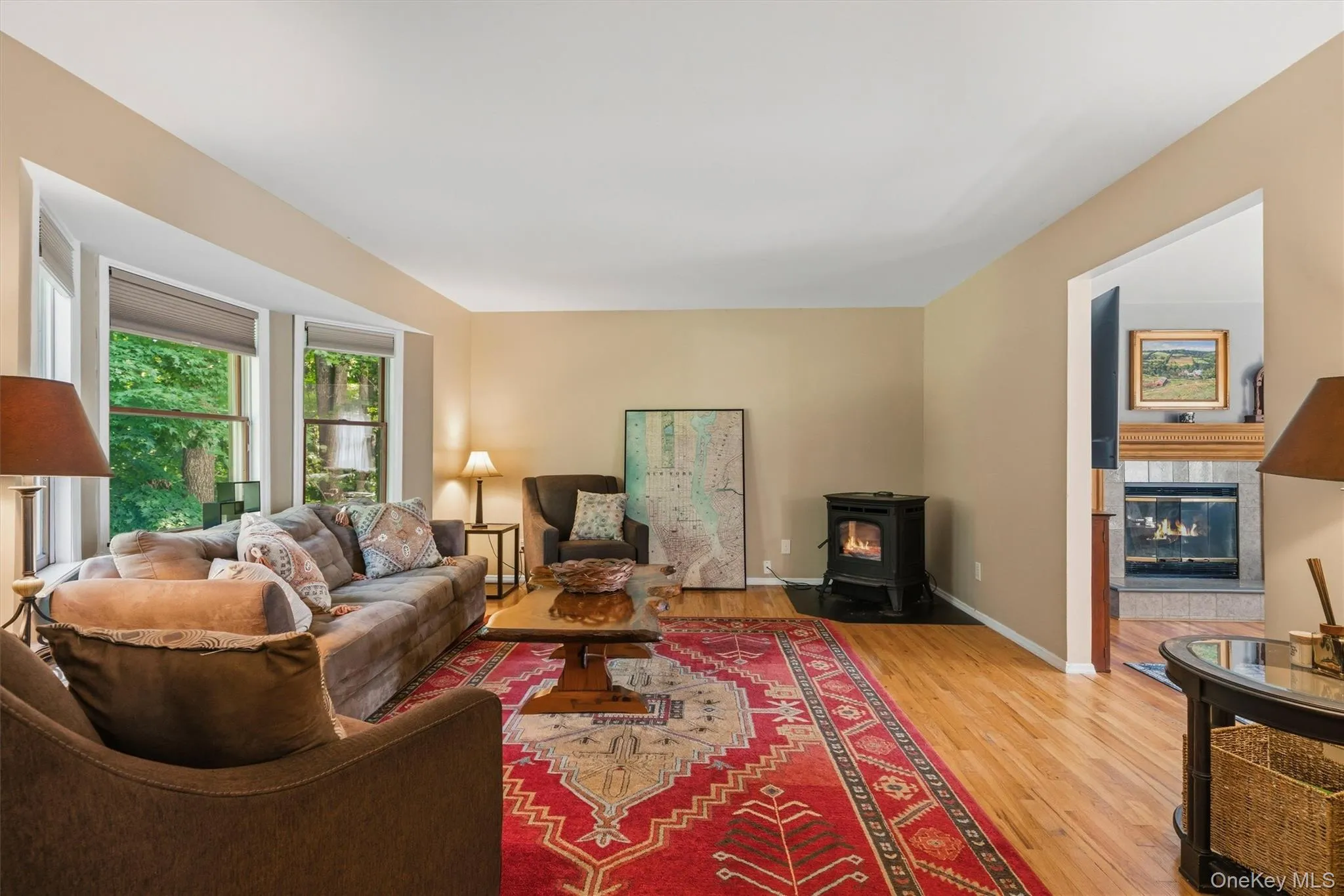 Bay window with multiple panes, wood-finish flooring, freestanding fireplace with a black hearth, and neutral wall tones Bay window with multiple panes, wood-finish flooring, freestanding fireplace with a black hearth, and neutral wall tones