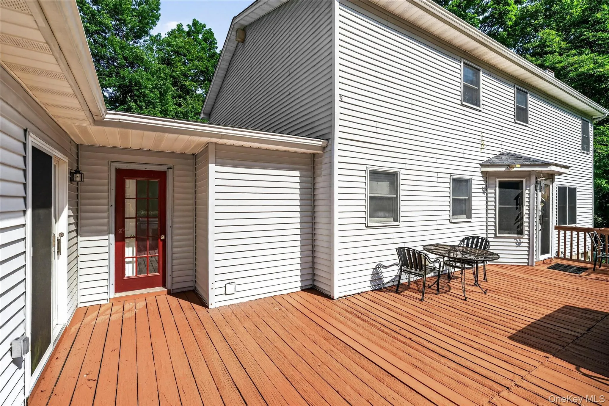 Expansive outdoor deck with rich wood-finish flooring, white siding, and multiple access points Expansive outdoor deck with rich wood-finish flooring, white siding, and multiple access points