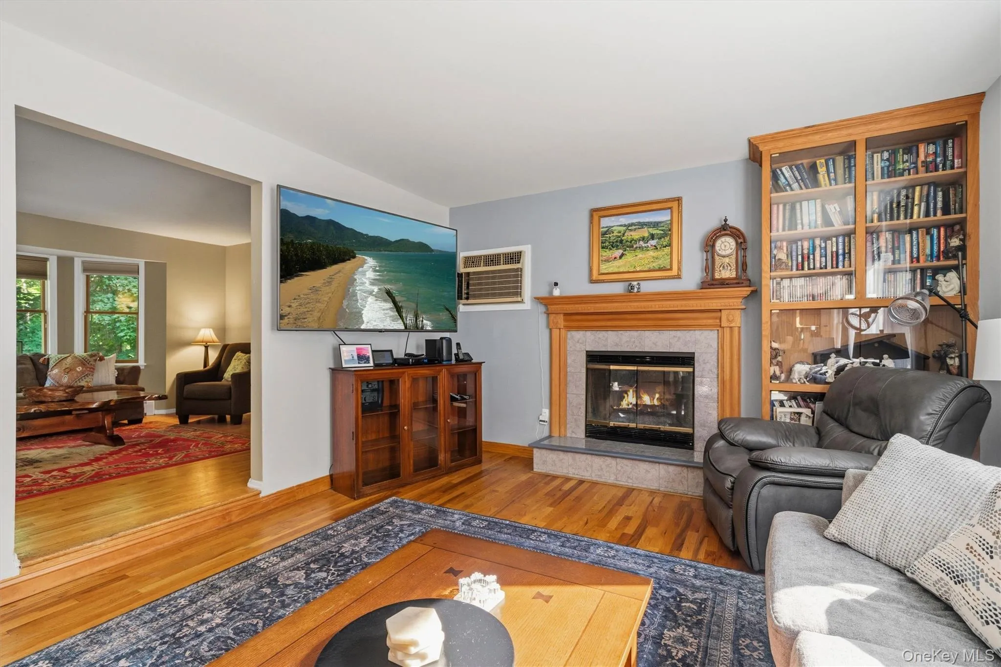 Hardwood flooring, wood-mantled fireplace with tile surround, built-in display cabinetry, and an open entryway to an additional room Hardwood flooring, wood-mantled fireplace with tile surround, built-in display cabinetry, and an open entryway to an additional room