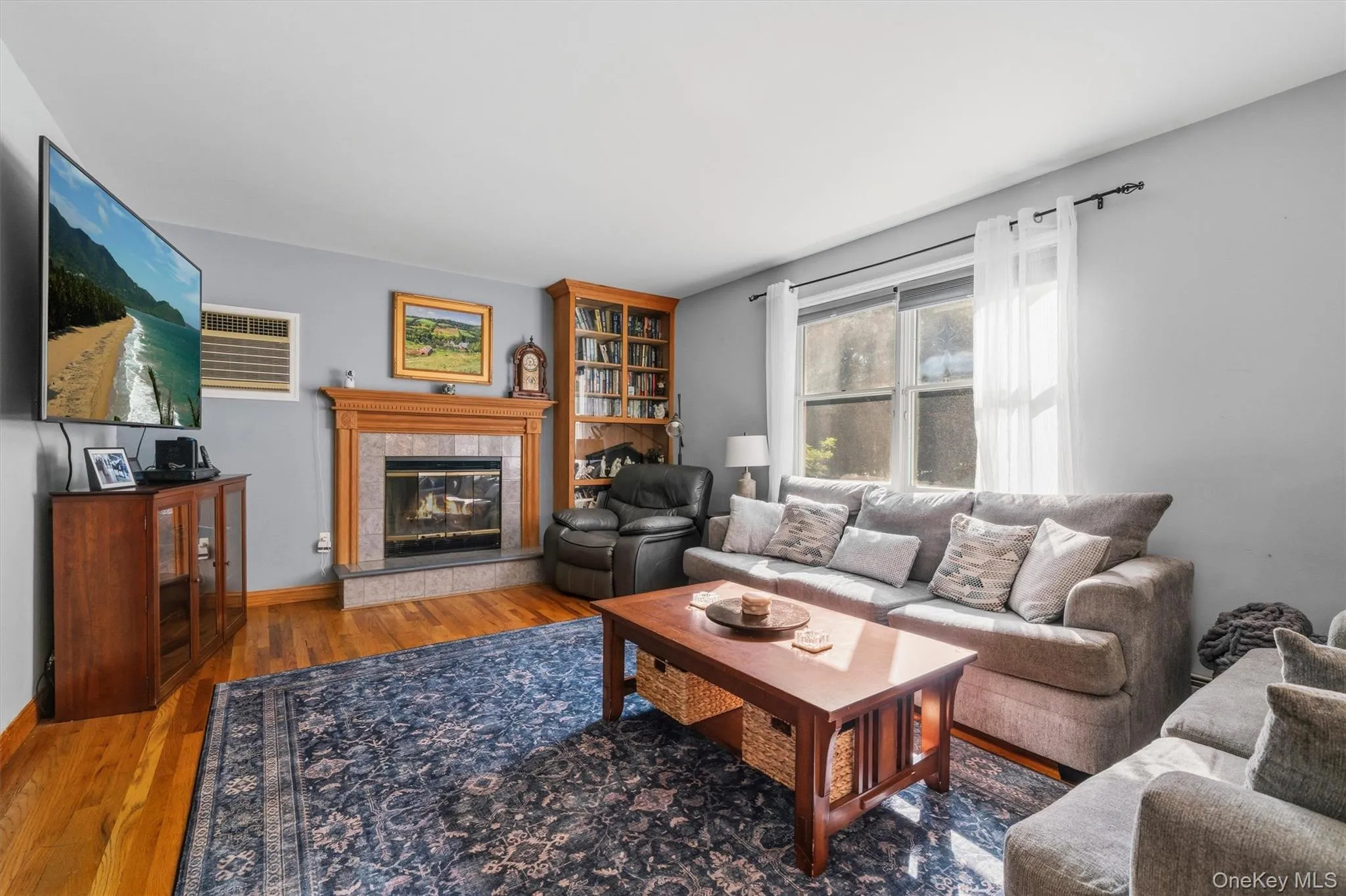 Hardwood flooring, fireplace with stone surround, built-in wooden bookcase, and window with sheer curtains Hardwood flooring, fireplace with stone surround, built-in wooden bookcase, and window with sheer curtains
