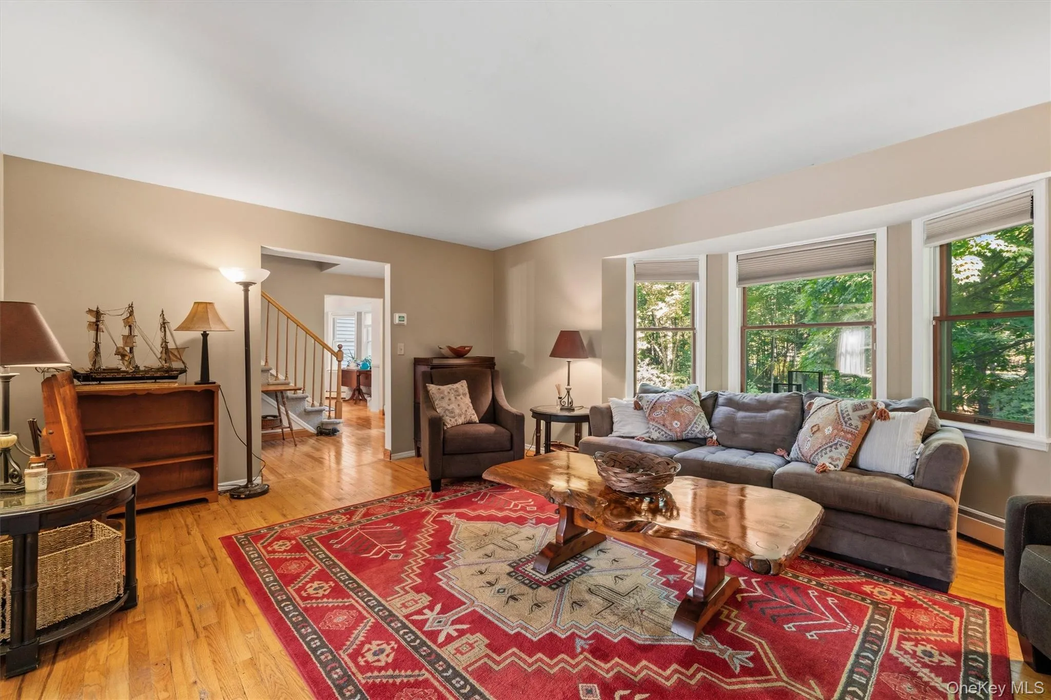 Hardwood flooring throughout, a bay window with multiple panes, a visible staircase with wood newel posts, and neutral wall tones Hardwood flooring throughout, a bay window with multiple panes, a visible staircase with wood newel posts, and neutral wall tones