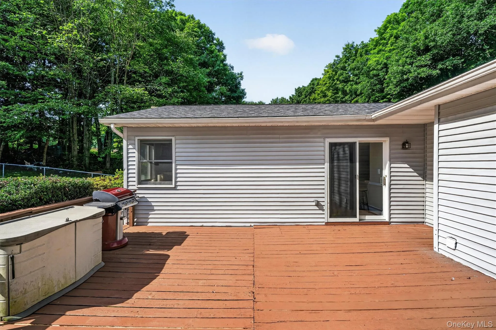 Expansive outdoor deck with wood-finish flooring, featuring light gray vinyl siding and a sliding glass door Expansive outdoor deck with wood-finish flooring, featuring light gray vinyl siding and a sliding glass door