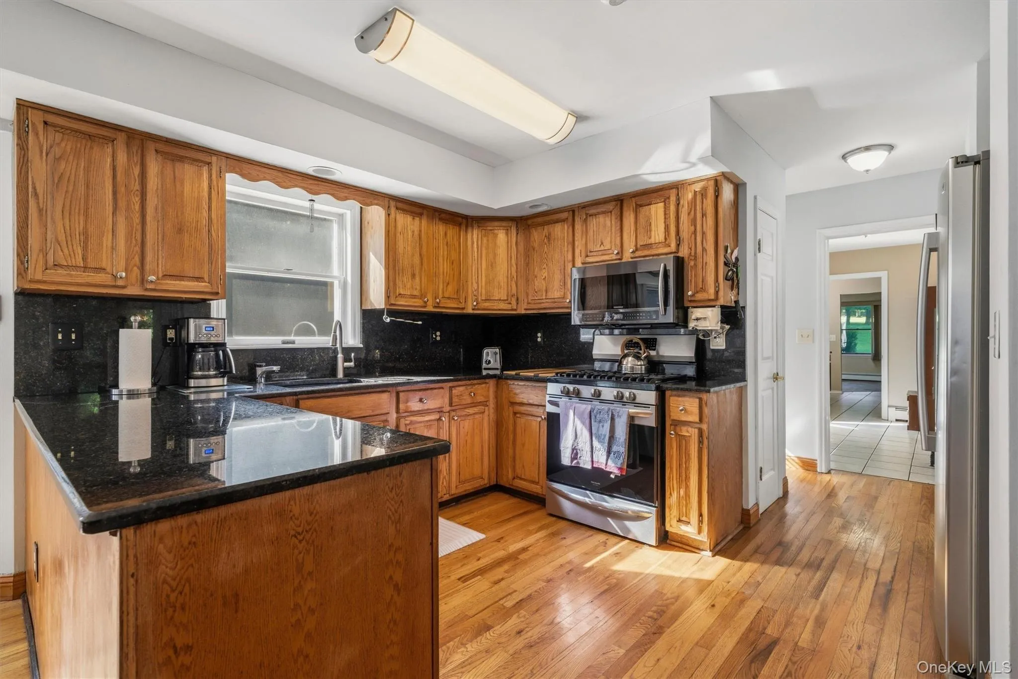 Kitchen featuring wood cabinetry, dark countertops, hardwood flooring, and stainless steel appliances Kitchen featuring wood cabinetry, dark countertops, hardwood flooring, and stainless steel appliances
