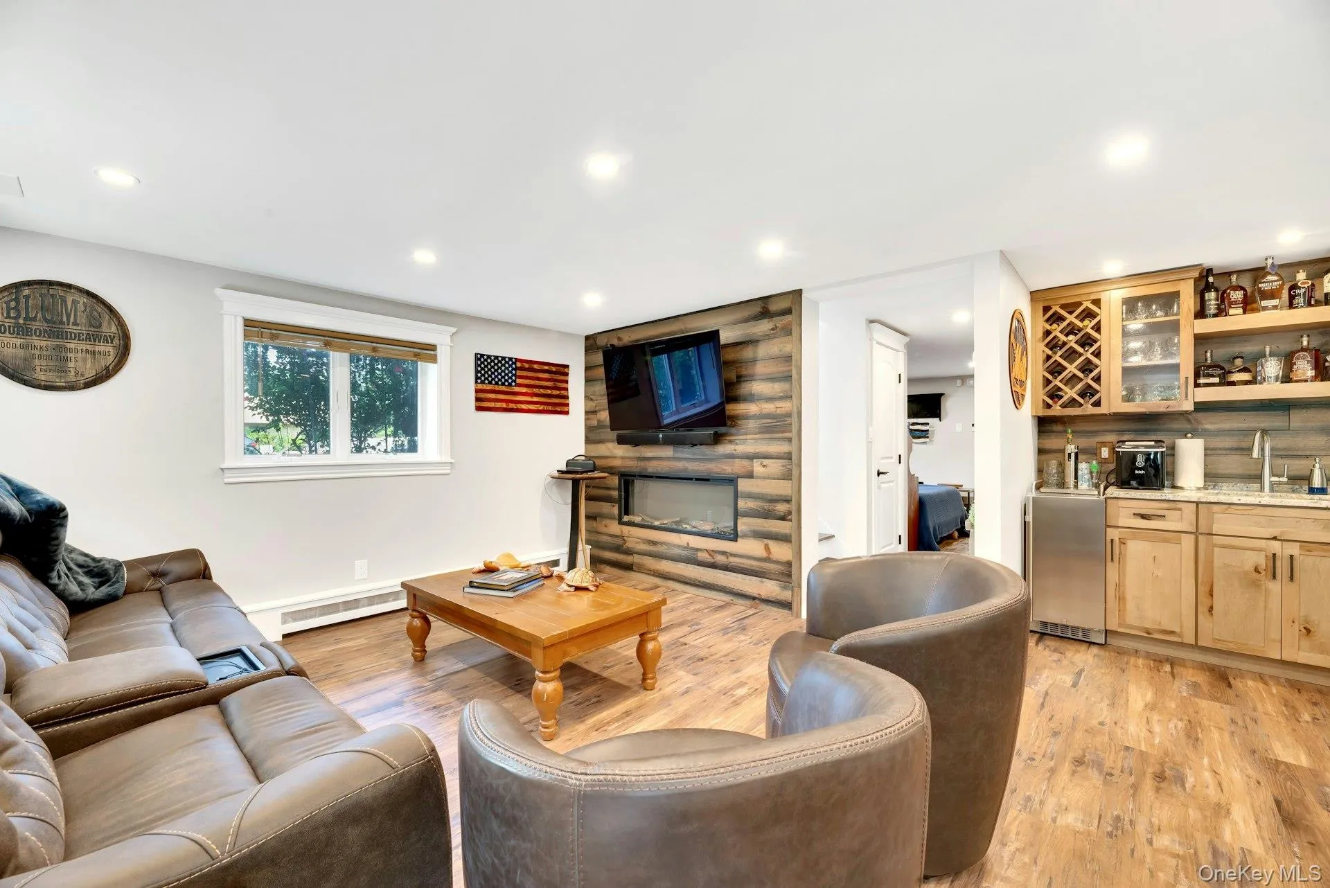Recessed lighting, wood-finish flooring, wood-paneled accent wall with built-in fireplace, wet bar with granite countertop, and natural wood cabinetry Recessed lighting, wood-finish flooring, wood-paneled accent wall with built-in fireplace, wet bar with granite countertop, and natural wood cabinetry