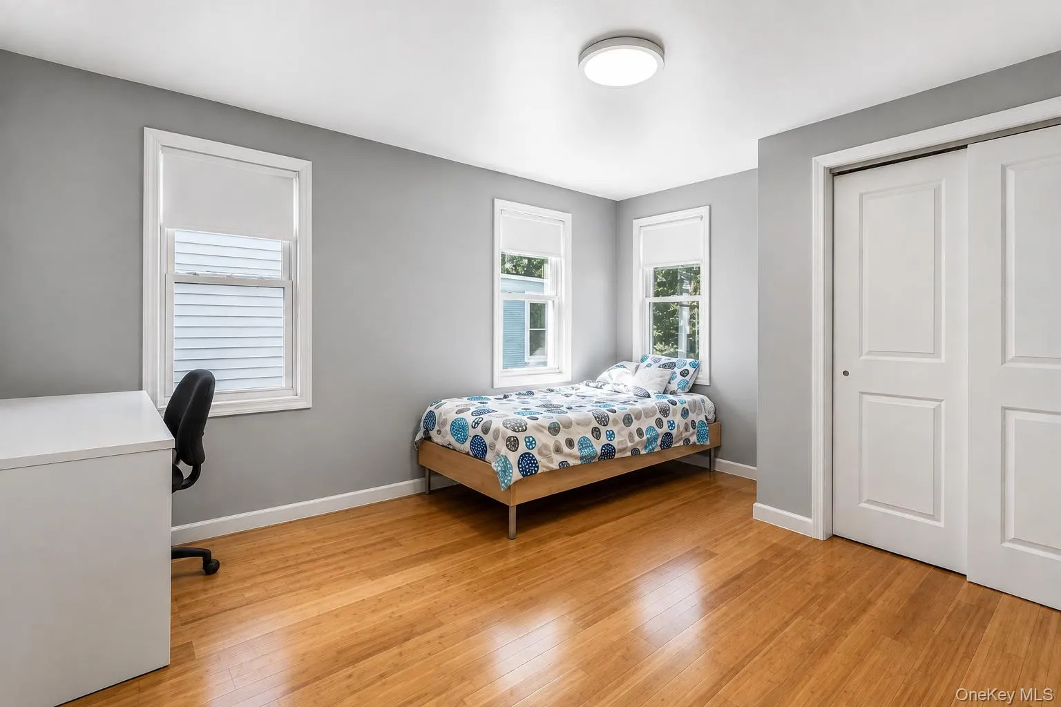 Hardwood flooring, painted walls, two windows with roller shades, and a flush mount ceiling light Hardwood flooring, painted walls, two windows with roller shades, and a flush mount ceiling light