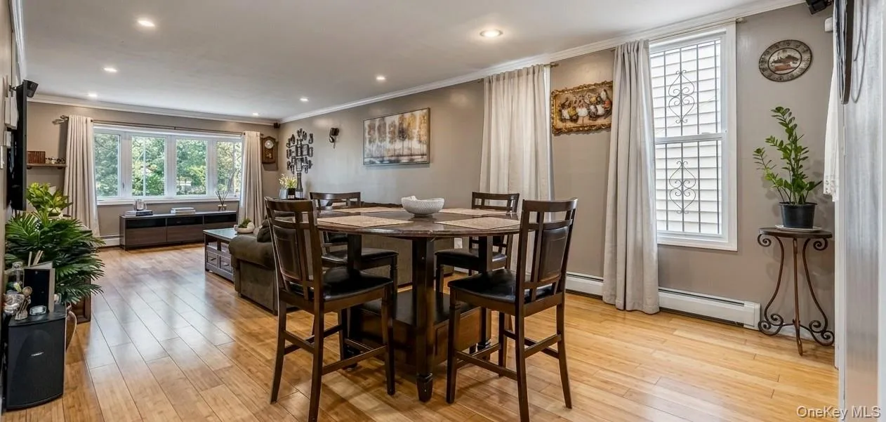 The spacious first-floor living and dining area features polished hardwood floors, modern recessed lighting, and clean neutral walls. A large round dining set sits comfortably in the foreground, flowing seamlessly into a bright, window-filled lounge area perfect for entertaining. The spacious first-floor living and dining area features polished hardwood floors, modern recessed lighting, and clean neutral walls. A large round dining set sits comfortably in the foreground, flowing seamlessly into a bright, window-filled lounge area perfect for entertaining.