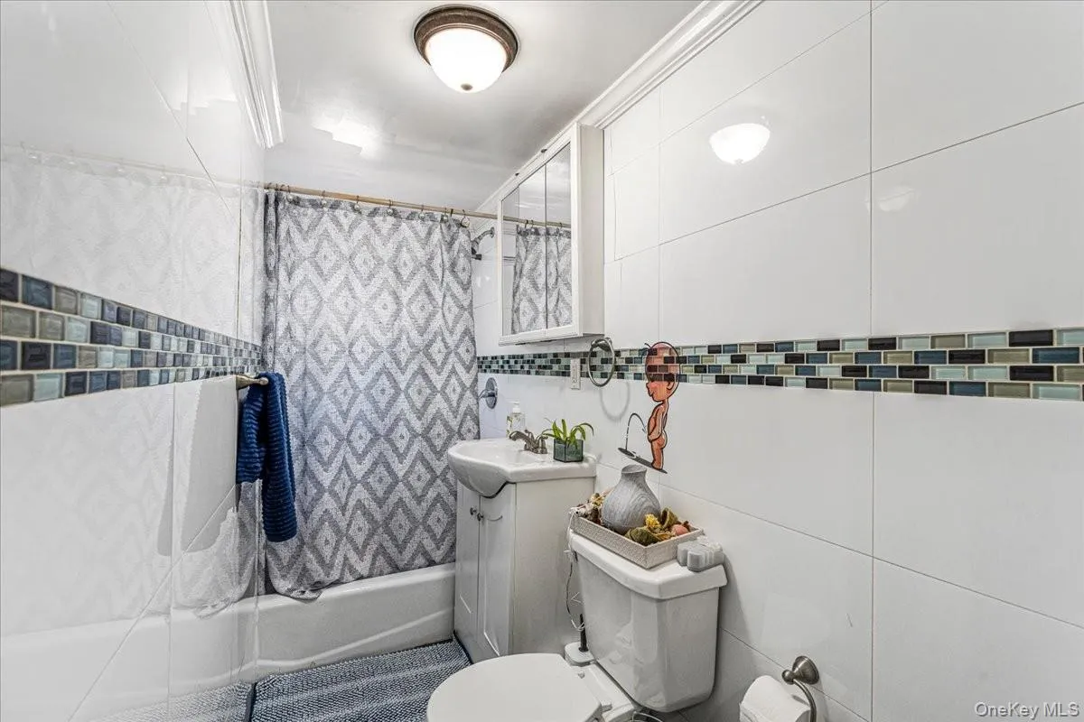 The first floor bathroom features bright white wall tiling accented by a stylish mosaic border that adds a modern touch. A compact pedestal sink and clean fixtures maximize the space, creating a fresh and efficient full bath. The first floor bathroom features bright white wall tiling accented by a stylish mosaic border that adds a modern touch. A compact pedestal sink and clean fixtures maximize the space, creating a fresh and efficient full bath.