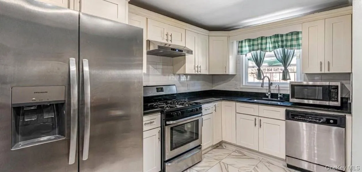 The first-floor kitchen features an open layout with bright marble-look flooring, crisp white cabinetry, and modern stainless steel appliances. A large matching refrigerator, built-in dishwasher, and a cozy dining island make this a highly functional and beautiful space. The first-floor kitchen features an open layout with bright marble-look flooring, crisp white cabinetry, and modern stainless steel appliances. A large matching refrigerator, built-in dishwasher, and a cozy dining island make this a highly functional and beautiful space.