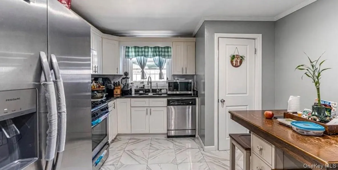 The first-floor kitchen features an open layout with bright marble-look flooring, crisp white cabinetry, and modern stainless steel appliances. A large matching refrigerator, built-in dishwasher, and a cozy dining island make this a highly functional and beautiful space. The first-floor kitchen features an open layout with bright marble-look flooring, crisp white cabinetry, and modern stainless steel appliances. A large matching refrigerator, built-in dishwasher, and a cozy dining island make this a highly functional and beautiful space.