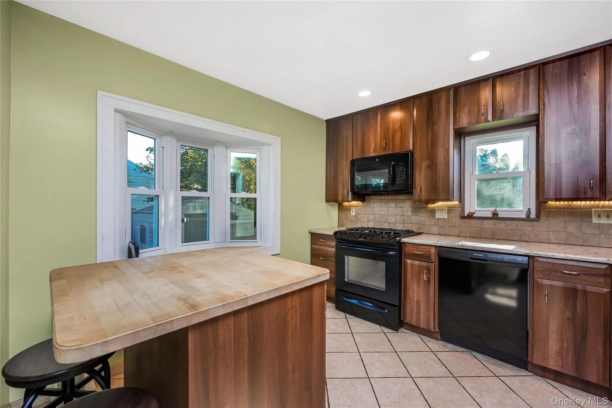 Kitchen featuring wood-finish cabinetry, black appliances, tile flooring, and a bay window Kitchen featuring wood-finish cabinetry, black appliances, tile flooring, and a bay window