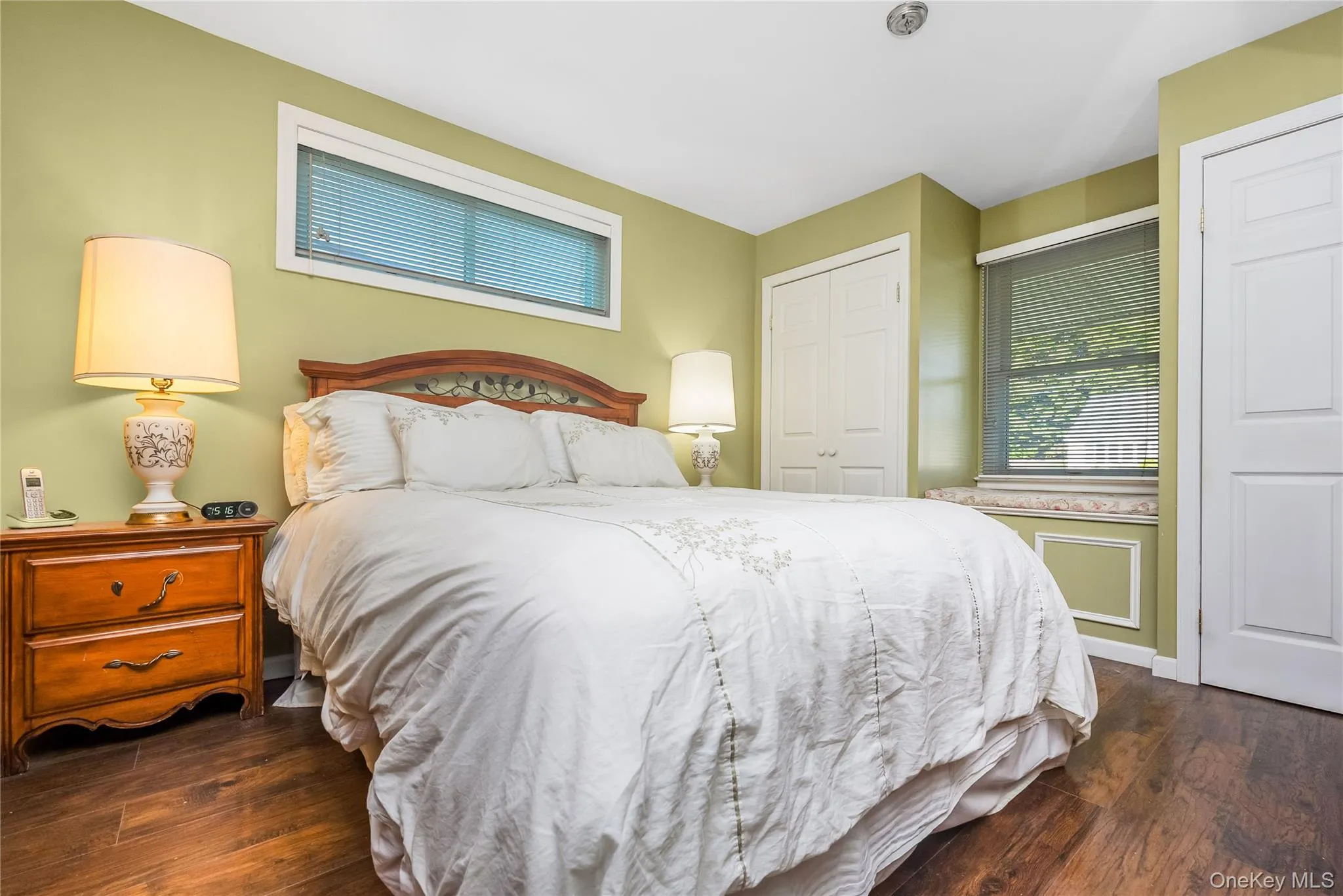 Master bedroom with Wood-finish flooring, two large windows with blinds, a window seat, and bi-fold closet doors Master bedroom with Wood-finish flooring, two large windows with blinds, a window seat, and bi-fold closet doors