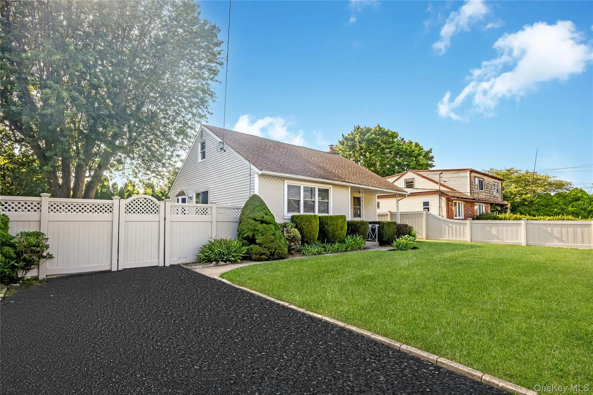 Paved driveway with white lattice-top fencing and gate, mature landscaping, and a manicured lawn Paved driveway with white lattice-top fencing and gate, mature landscaping, and a manicured lawn