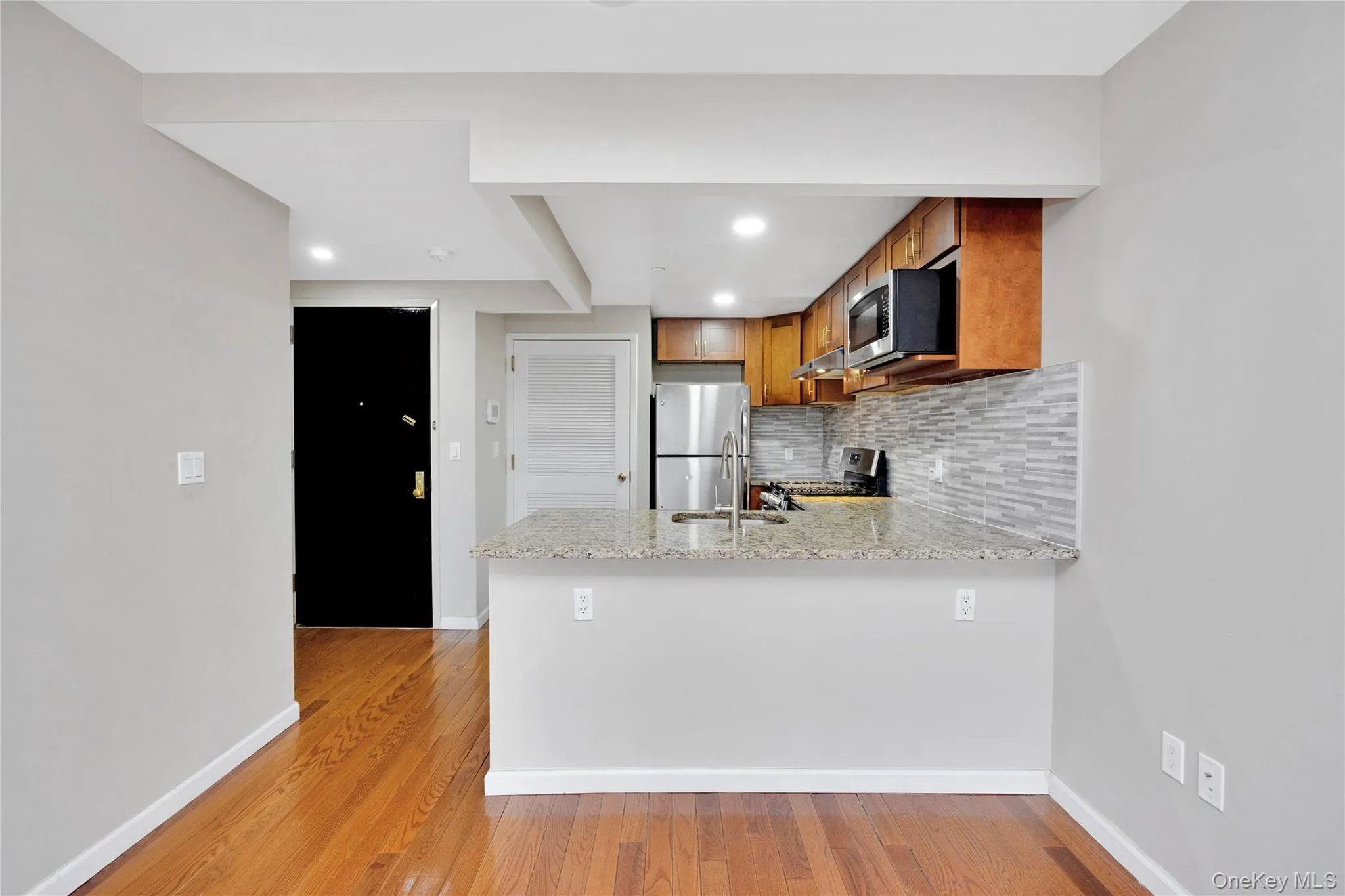 Kitchen featuring baseboards, a peninsula, backsplash, brown cabinets, and appliances with stainless steel finishes Kitchen featuring baseboards, a peninsula, backsplash, brown cabinets, and appliances with stainless steel finishes