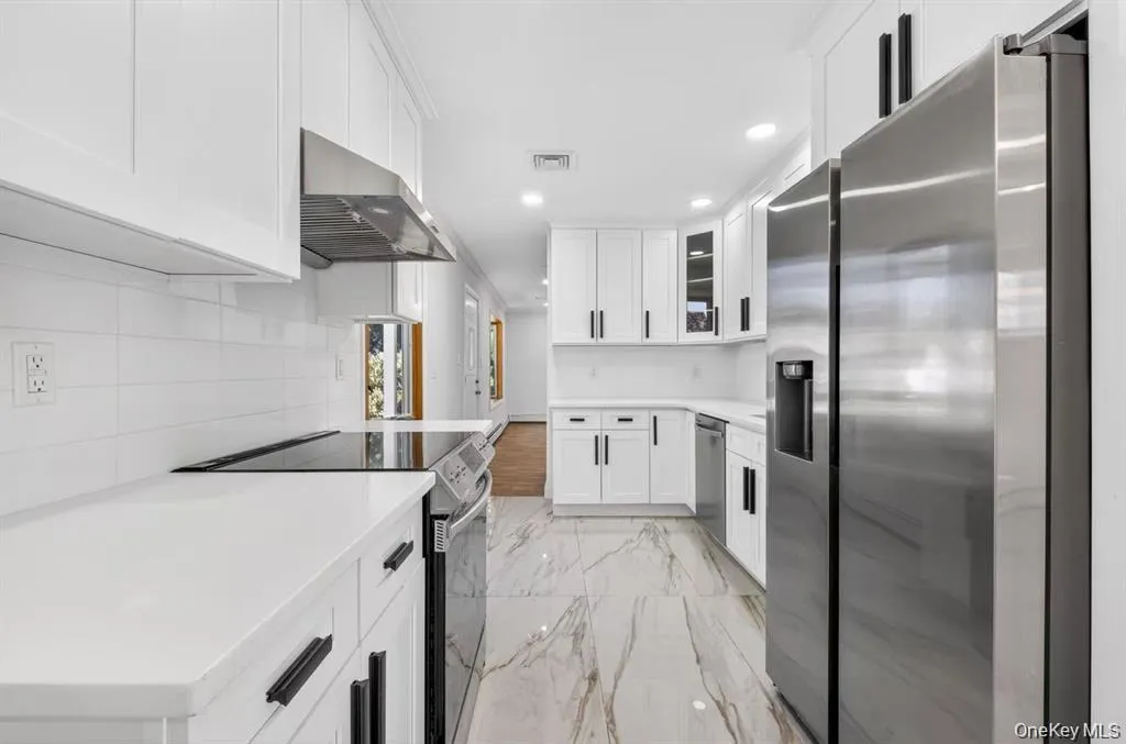 Modern kitchen featuring white shaker cabinetry, stainless steel appliances, white countertops, and a white subway tile backsplash Modern kitchen featuring white shaker cabinetry, stainless steel appliances, white countertops, and a white subway tile backsplash
