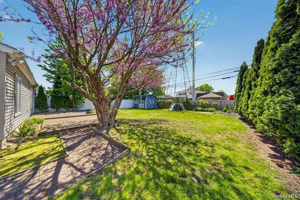 Expansive backyard with a manicured lawn, established flowering tree, stone patio, and privacy hedging Expansive backyard with a manicured lawn, established flowering tree, stone patio, and privacy hedging