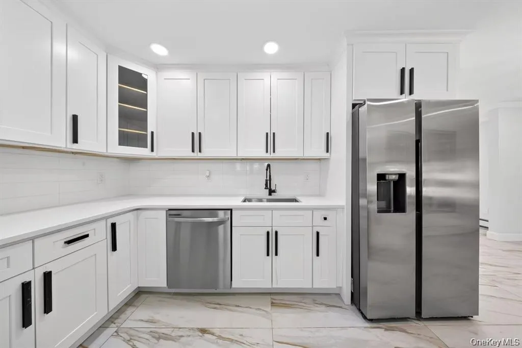 Contemporary kitchen featuring white cabinetry with matte black hardware, white countertops, a tiled backsplash, and stainless steel appliances Contemporary kitchen featuring white cabinetry with matte black hardware, white countertops, a tiled backsplash, and stainless steel appliances