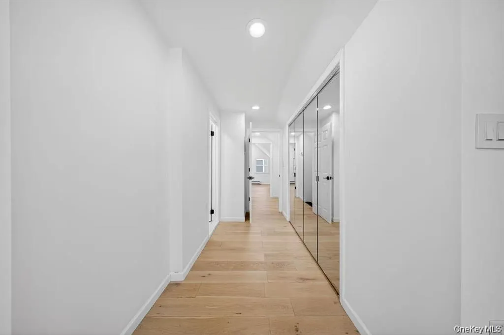 Recessed lighting illuminating a hallway with wood-finish flooring and a mirrored wall Recessed lighting illuminating a hallway with wood-finish flooring and a mirrored wall