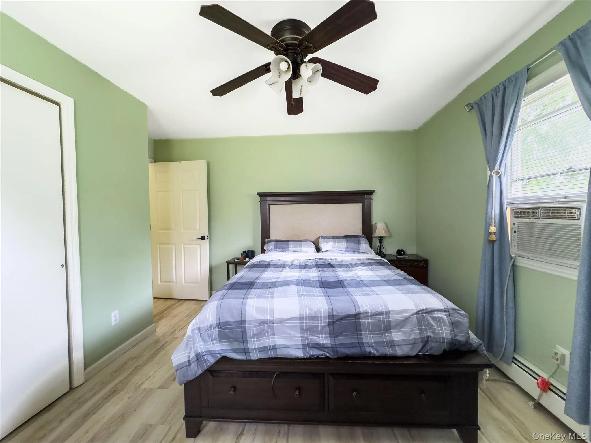 Bright secondary bedroom featuring soft green walls, wood-finish flooring, and a black ceiling fan with integrated lighting Bright secondary bedroom featuring soft green walls, wood-finish flooring, and a black ceiling fan with integrated lighting