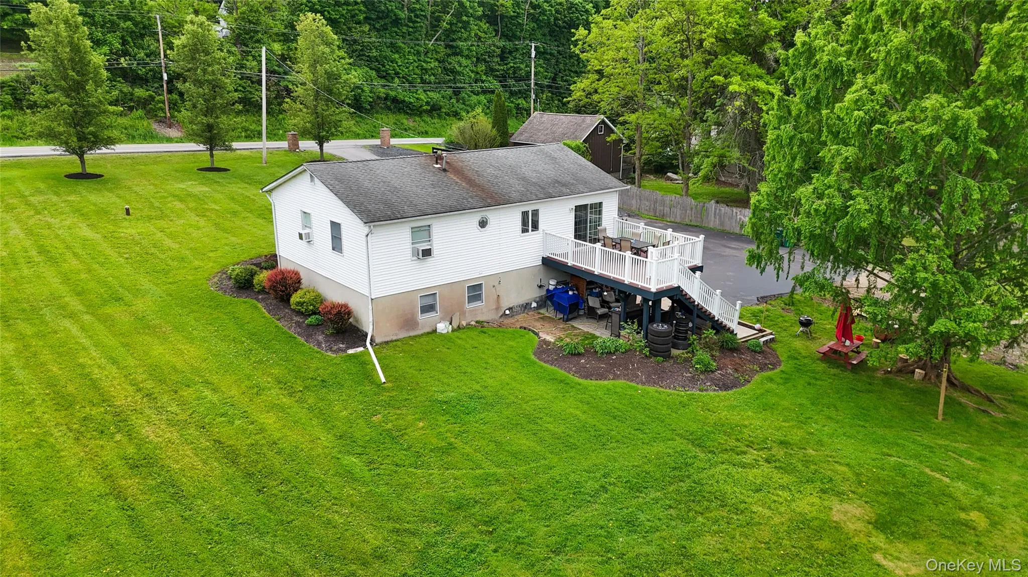 Expansive green lawn, multi-level exterior deck, white siding, landscaping with shrubs, mature trees Expansive green lawn, multi-level exterior deck, white siding, landscaping with shrubs, mature trees