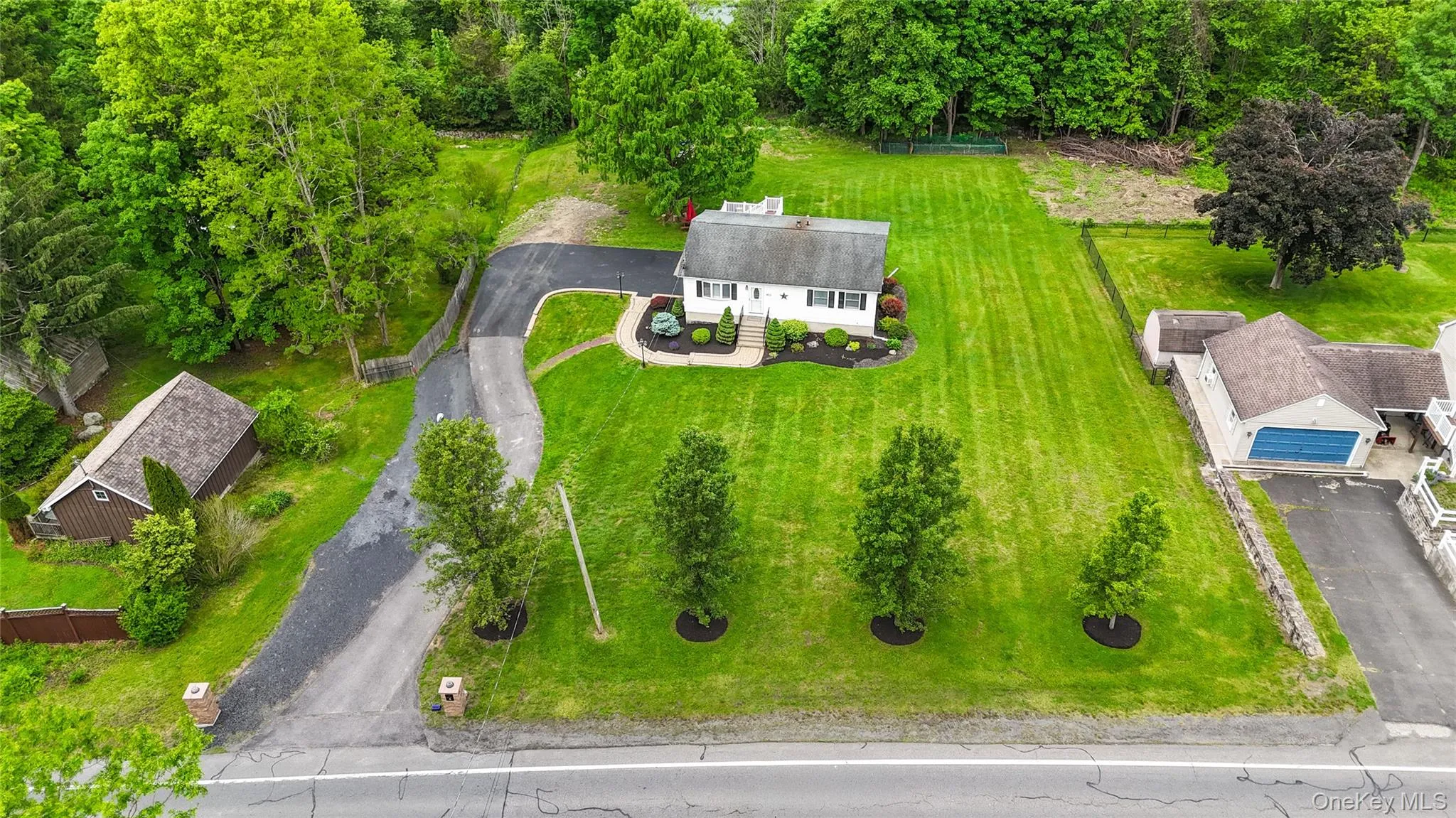 Sprawling residential property featuring a pristine manicured lawn with symmetrical landscape plantings, a curved asphalt driveway, and mature tree-lined perimeter Sprawling residential property featuring a pristine manicured lawn with symmetrical landscape plantings, a curved asphalt driveway, and mature tree-lined perimeter