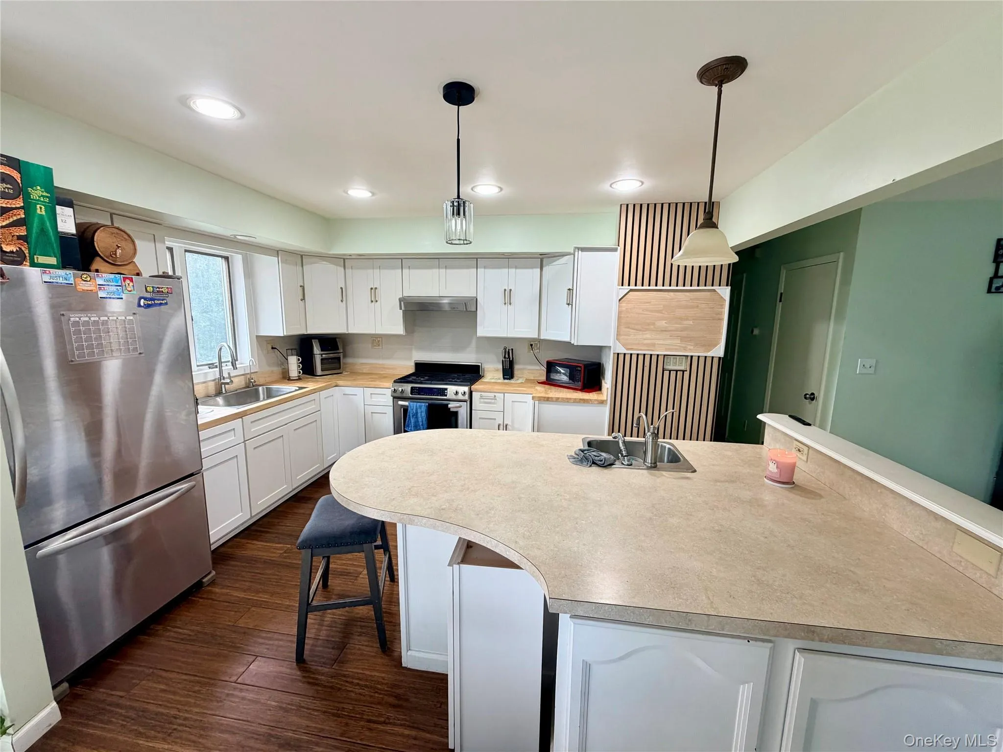 Modern kitchen featuring white cabinetry, stainless steel appliances, and a large quartz countertop island with seating Modern kitchen featuring white cabinetry, stainless steel appliances, and a large quartz countertop island with seating