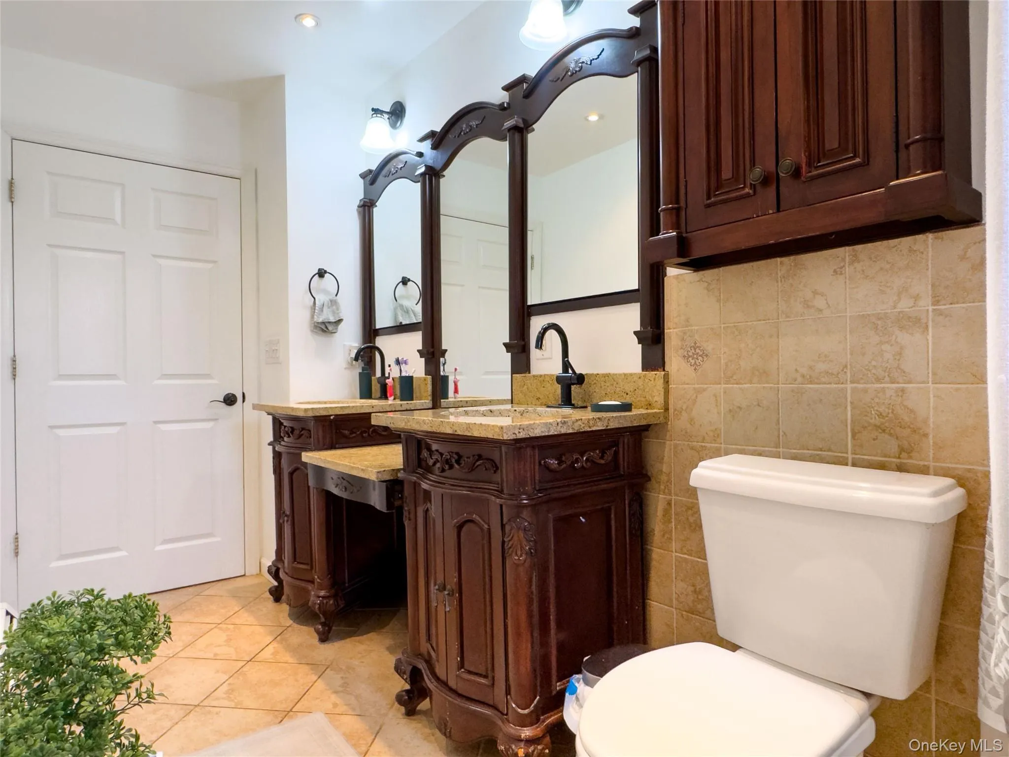 Dual vanity sinks with granite countertops, ornate wood cabinetry, wall-mounted mirrors, and tiled flooring Dual vanity sinks with granite countertops, ornate wood cabinetry, wall-mounted mirrors, and tiled flooring