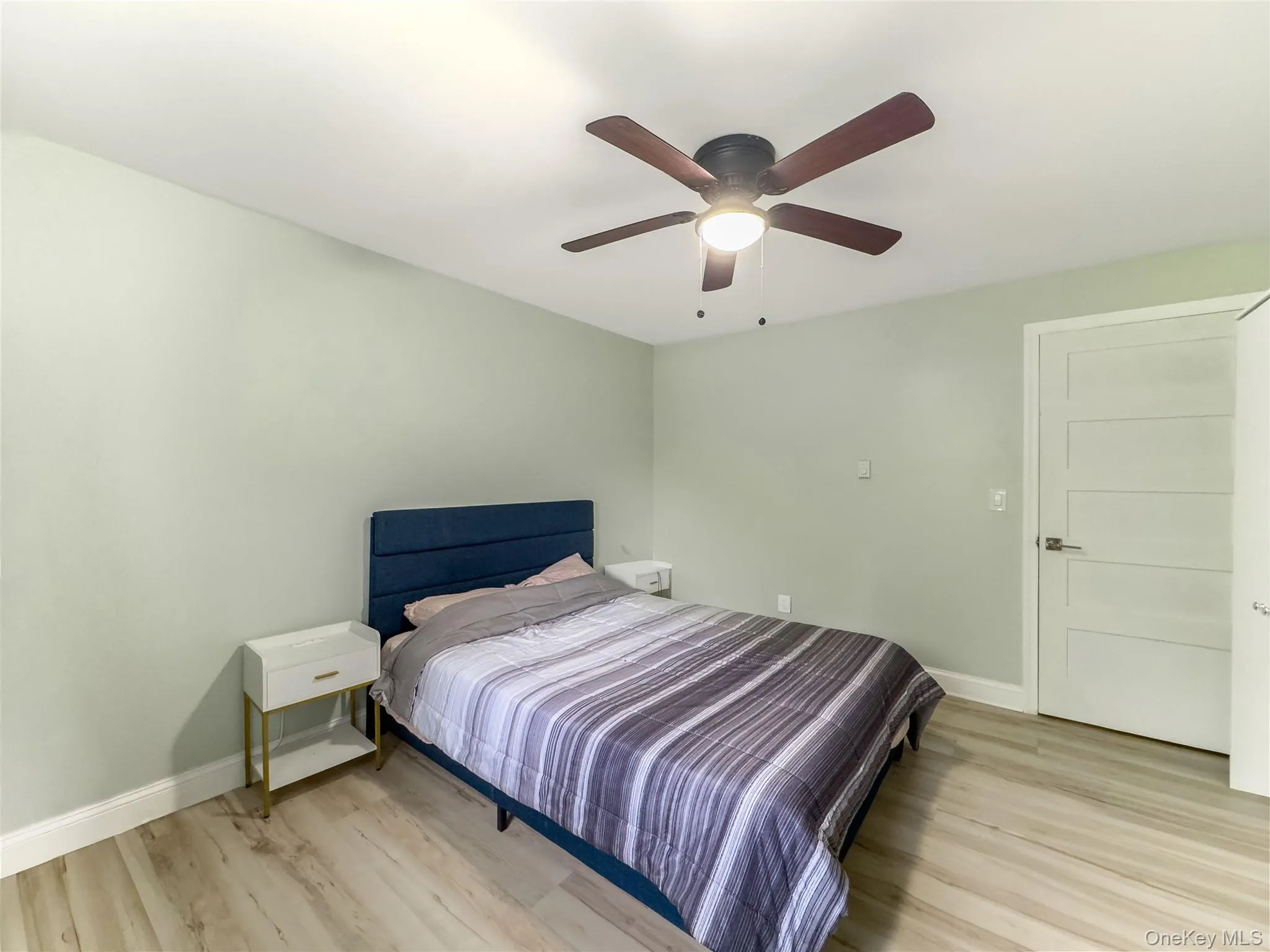 Bright secondary bedroom featuring a wood-finish plank floor, soft sage green walls, and a ceiling fan with integrated lighting Bright secondary bedroom featuring a wood-finish plank floor, soft sage green walls, and a ceiling fan with integrated lighting